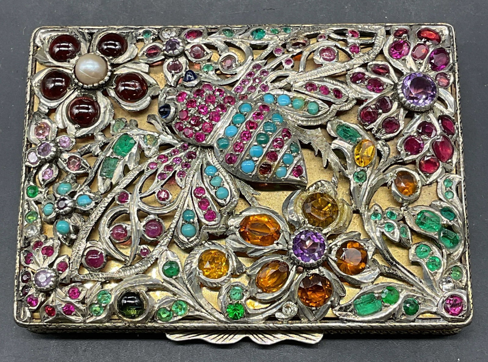 Vintage 800 Silver Jeweled Insect Compact Italy: Vintage 800 silver powder compact/box. Heavily jeweled lid with insect and flower motifs. Round and faceted colored stones and pearl. Gold plated interior. Mirror on interior. Chased ornate scroll cas