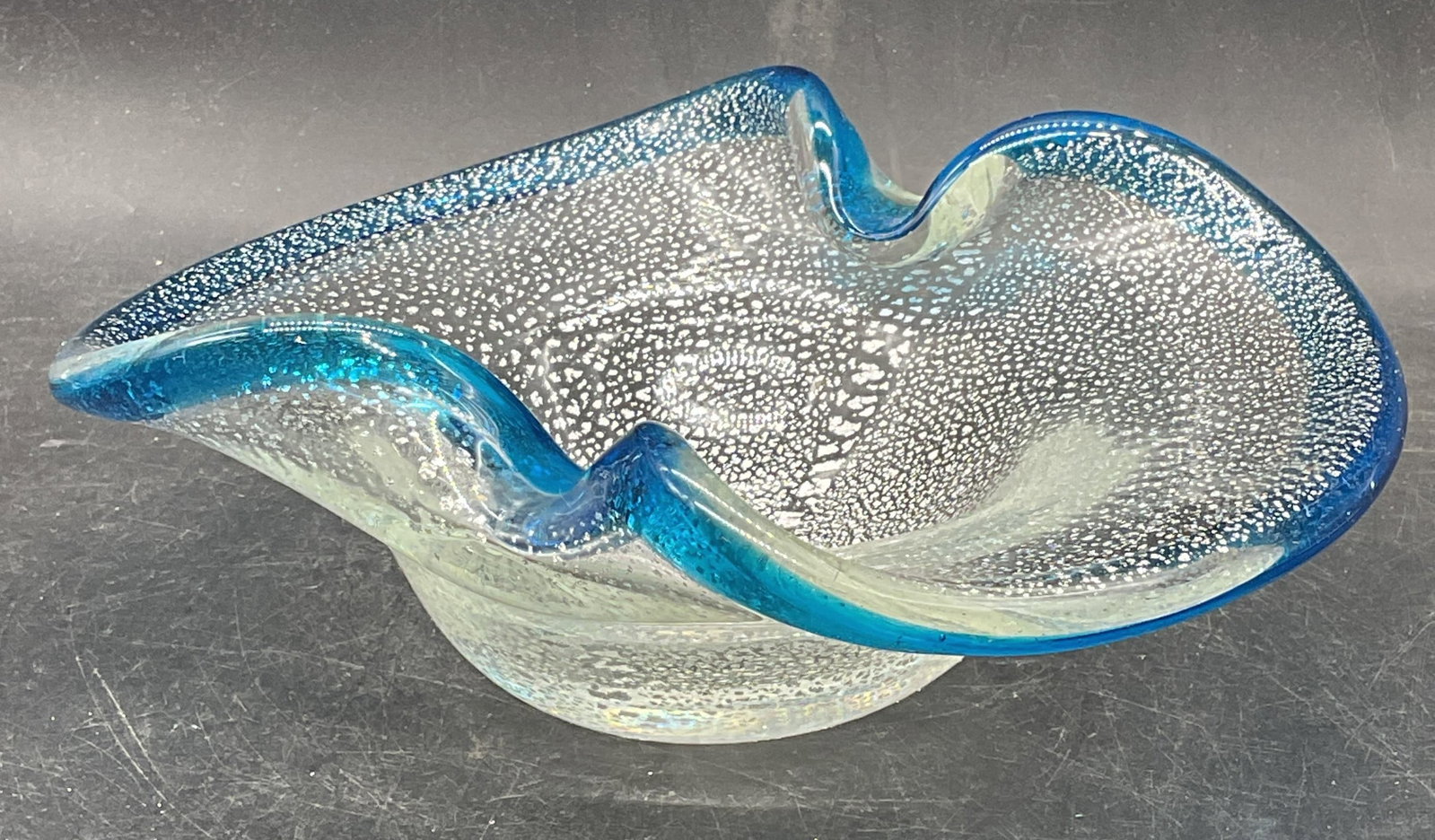MURANO Art Glass Clear Blue Silver Fleck Bowl: Vintage Murano hand blown art glass bowl with clear glass and silver fleck design and blue rim. Made in Italy, partial label on underside. Measures approx. 8.25 x 6 x 3 inches. Some scratching. Art