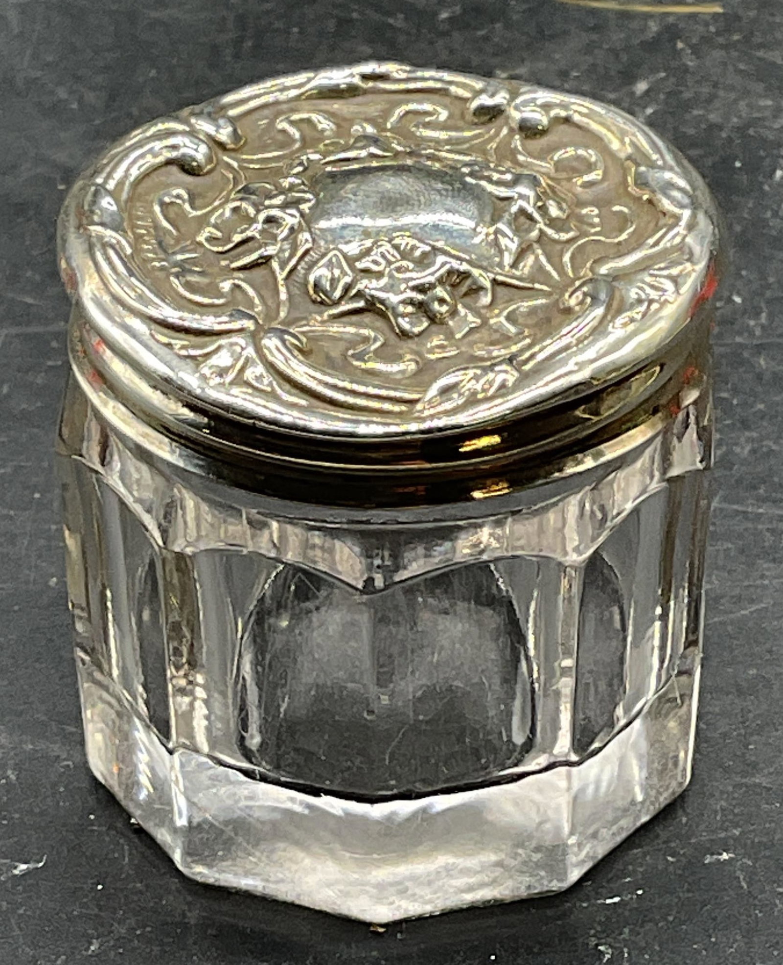 Vintage Sterling Silver Paneled Glass Jar: Vintage paneled glass jar with sterling silver lid. Ornate repousse floral lid. Marked sterling. Total weight of sterling 3.1 grams. Measures approx. 1.5 x 1.25 inches. Wear including scratching,