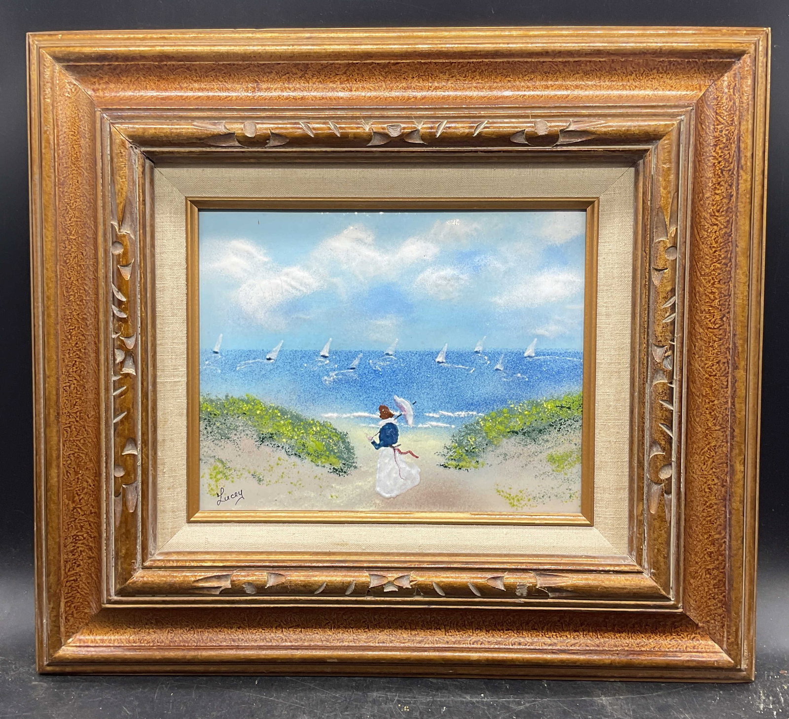 Signed Jean Lucey Beach Folk Enamel Painting: Framed enamel on metal folk art painting. Signed lower left, Lucey. Jean Lucey (American, 1925-2024). Beach scene with woman holding parasol. Decorative gilt wood frame. Not examined out of frame.