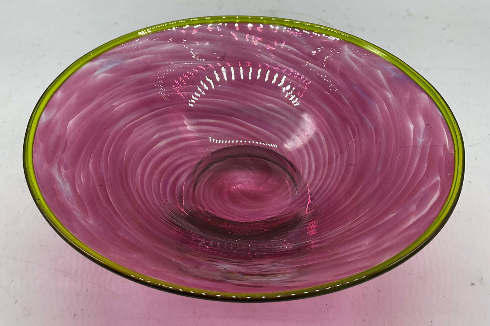 SGND Hand Blown Pink Art Glass Pedestal Bowl: Signed hand blown pink art glass pedestal bowl. Signed on underside, reads illegibly. Clear pedestal base. Wide pink bowl with green yellow tinted rim. Swirled design. Measures ht approx 3 inches diam