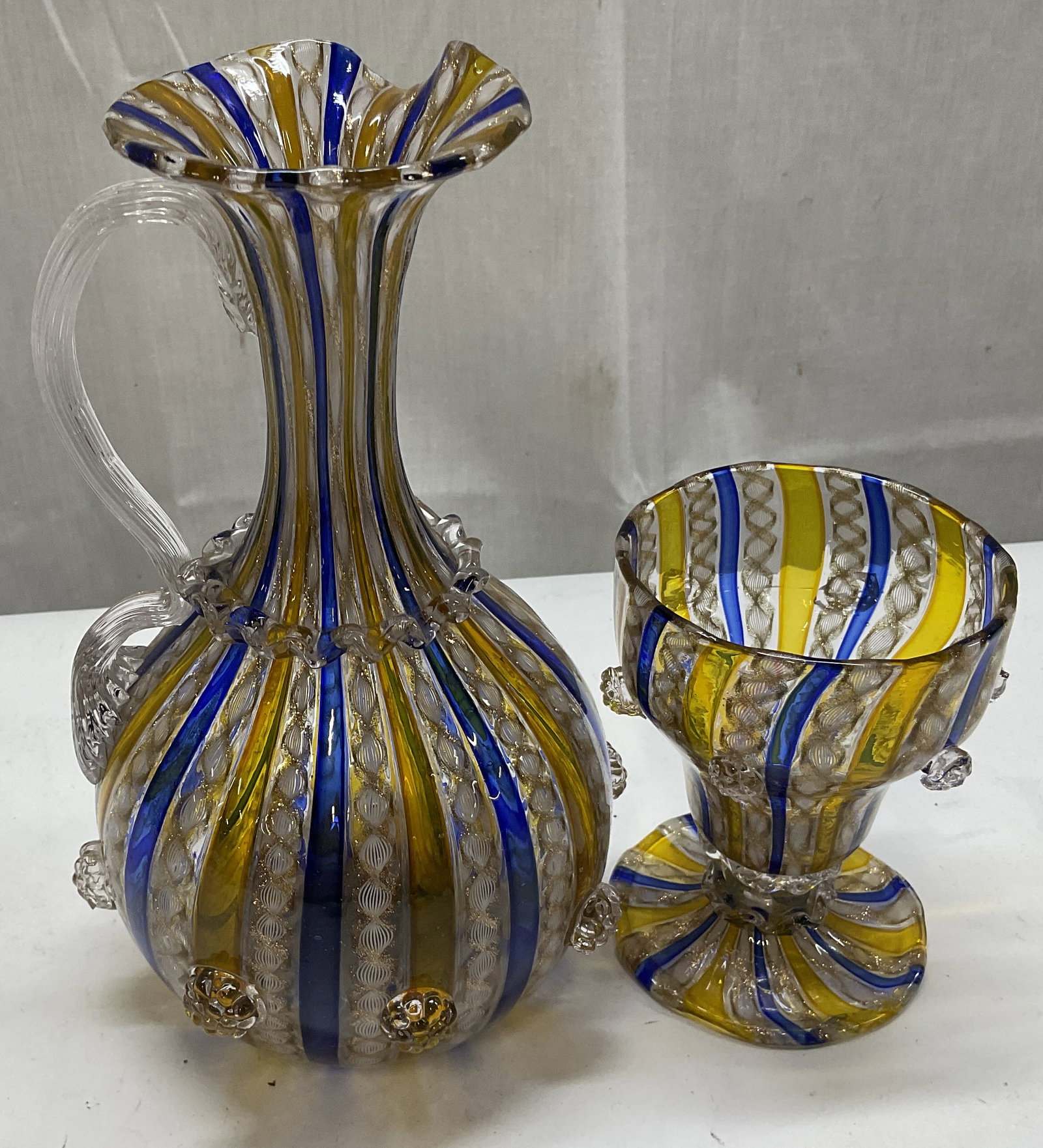 St2 VTG Venetian-Style Art Glass Pitcher & Goblet: Vintage Venetian-Style Blue and Yellow Striped Art Glass Pitcher and Goblet. Zanfirico Striped Glass Technique with Applied Glass Prunts. Gilt Accents. Visible Chip Present. Pitcher Measures app 7in