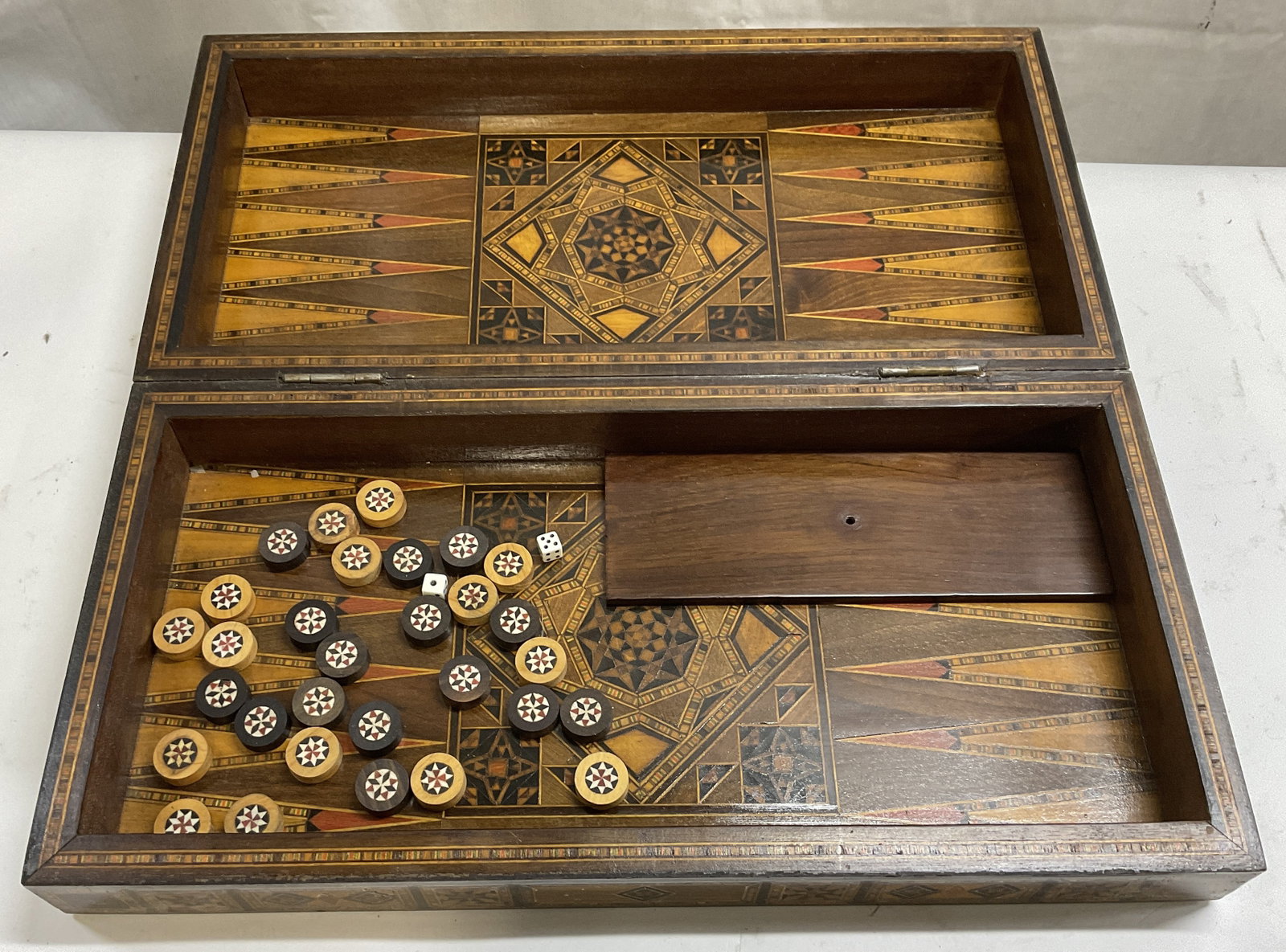 Syrian Marquetry Inlaid Backgammon Board: Syrian Marquetry Folding Backgammon Board. Crafted From Wood with Intricate Mother-Of-Pearl and Satinwood Inlay. Some Scratching. Comes with 30 Pieces and 2 Die. Measures app 3.25in H x 16in L. Syrian