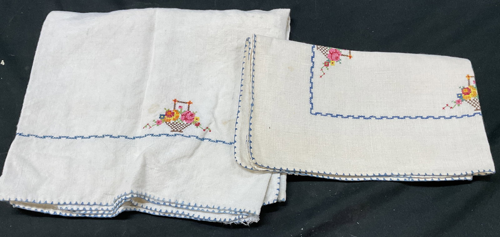 Set 2 Vtg White Embroidered Table Linens: Set of 2 vintage white embroidered table linens. Blue border. Embroidered floral basket motif in varying colors. Blue stitched trim. Size vary. Largest measures approx 16 x 37 inches. Some blemishes.