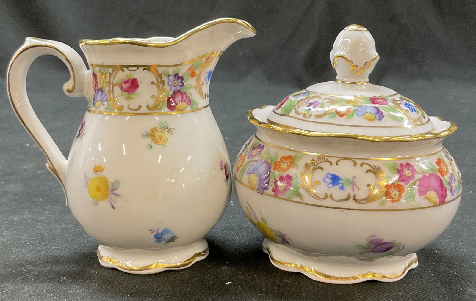 Set 2 Schumann Creamer & Sugar Bowl Germany: Set of 2 Schumann porcelain creamer and lidded sugar bowl. Marked on underside, reads Schumann Bavaria Germany US Zone. Scalloped gilt edge. Floral motifs in varying colors. Gilt accents. Measures ht