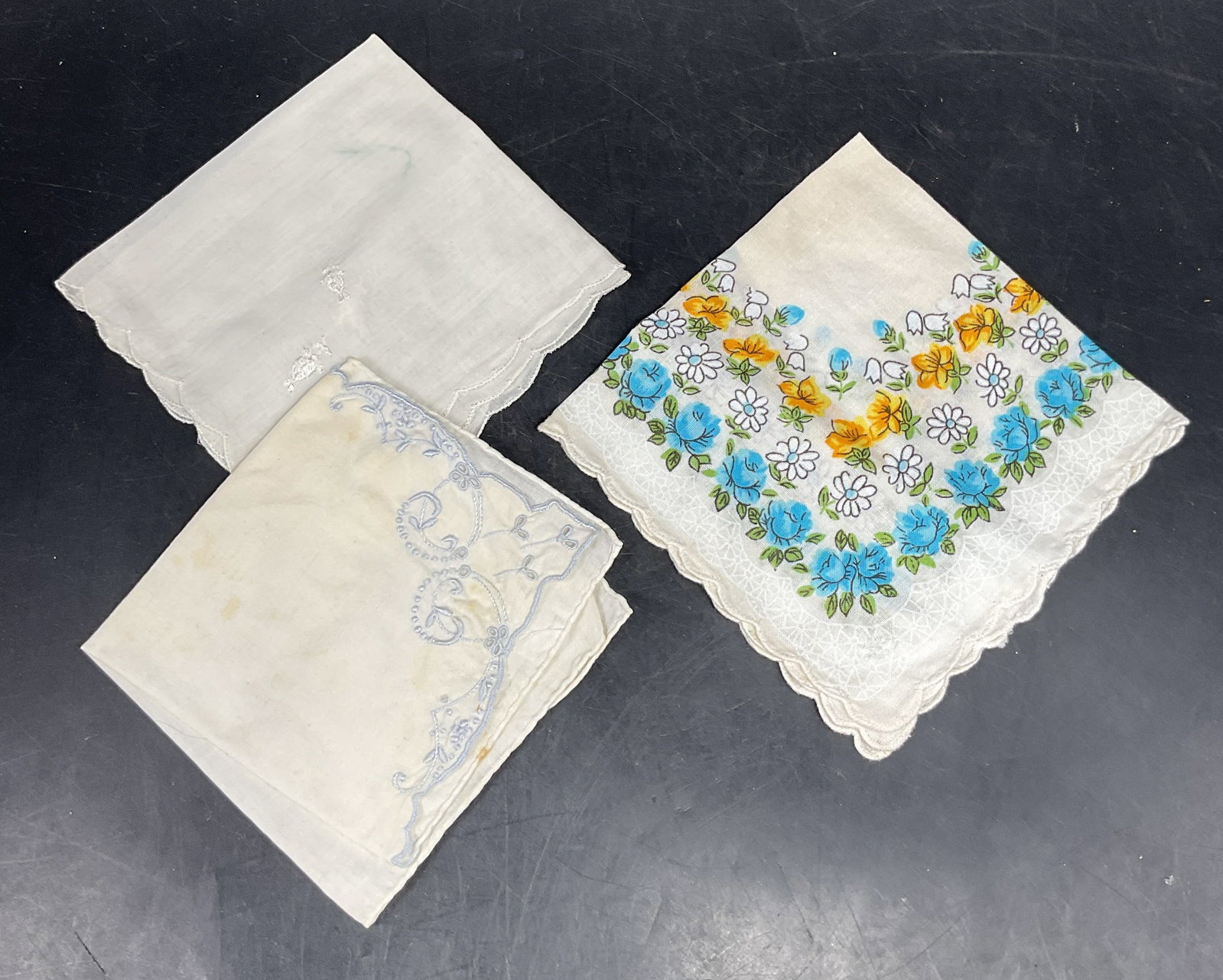 Lot 3 Vtg Floral, Embroidered Cotton Handkerchiefs: Lot of 3 vintage white cotton handkerchiefs. Blue embroidered, white embroidered, and floral print designs. Largest measures approx. 11 x 11 inches. Some blemishes and wear to all. Vintage handkerchie