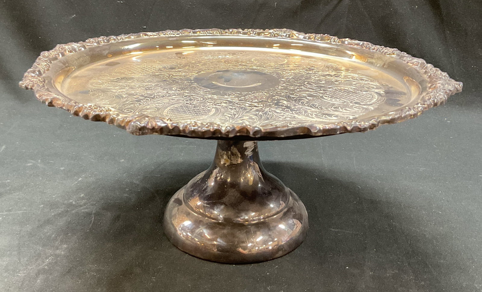 Sheridan Silver Plated Cake Stand: Sheridan Silver Plated cake stand. Marked on underside. Round pedestal base. Round plate. Ornate scalloped edges. Embossed scroll and floral motifs. Measures ht approx 5.5 inches diam approx 13 inches