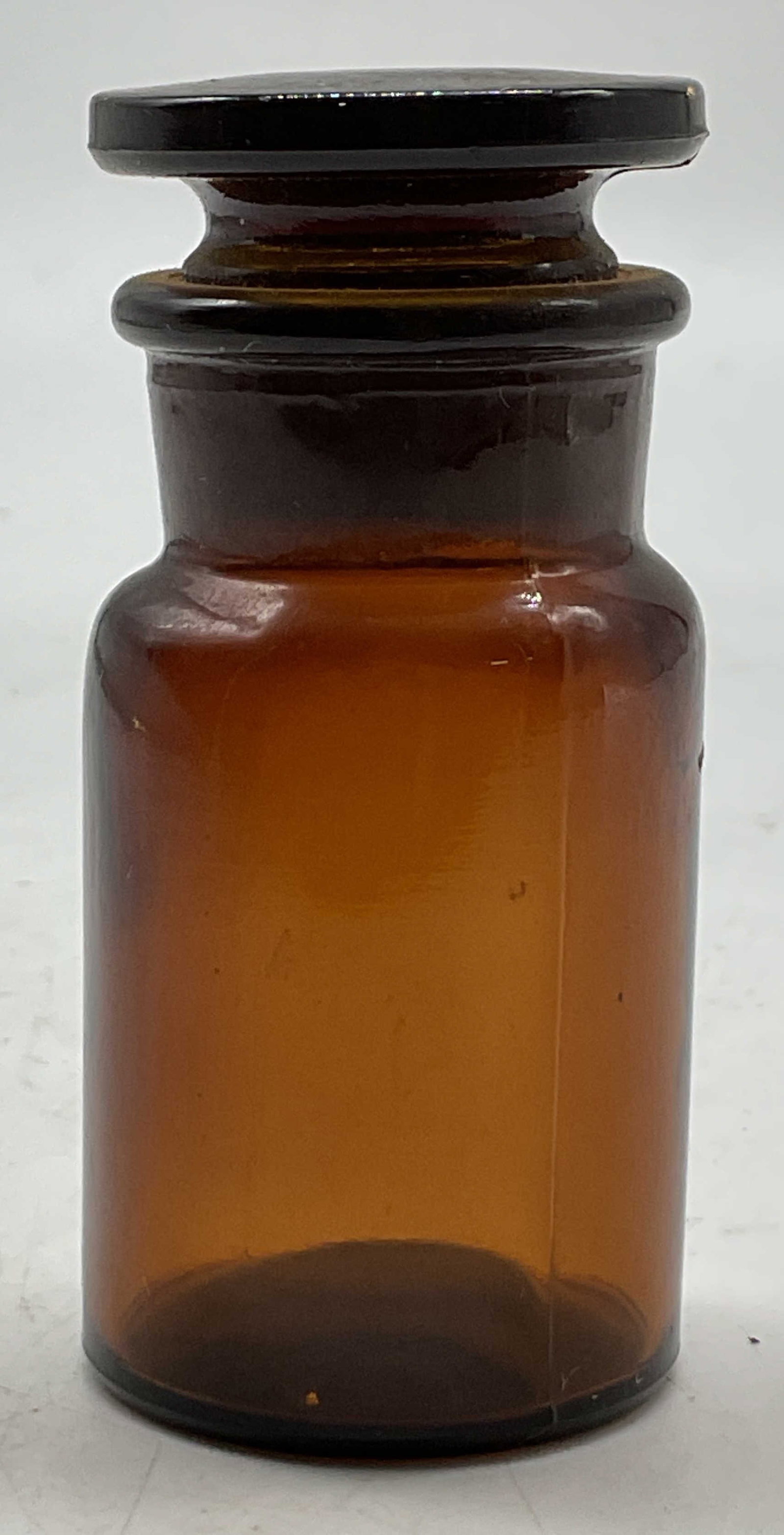T.C.W Co Brown Apothecary Jar W Stopper USA: T.C.W Co brown apothecary jar. Marked on underside. Made in USA. Comes with round stopper. Round shape. Measures ht approx 3 inches diam approx 1.5 inches. Scratching. Apothecary jar, T.C.W Co, home d