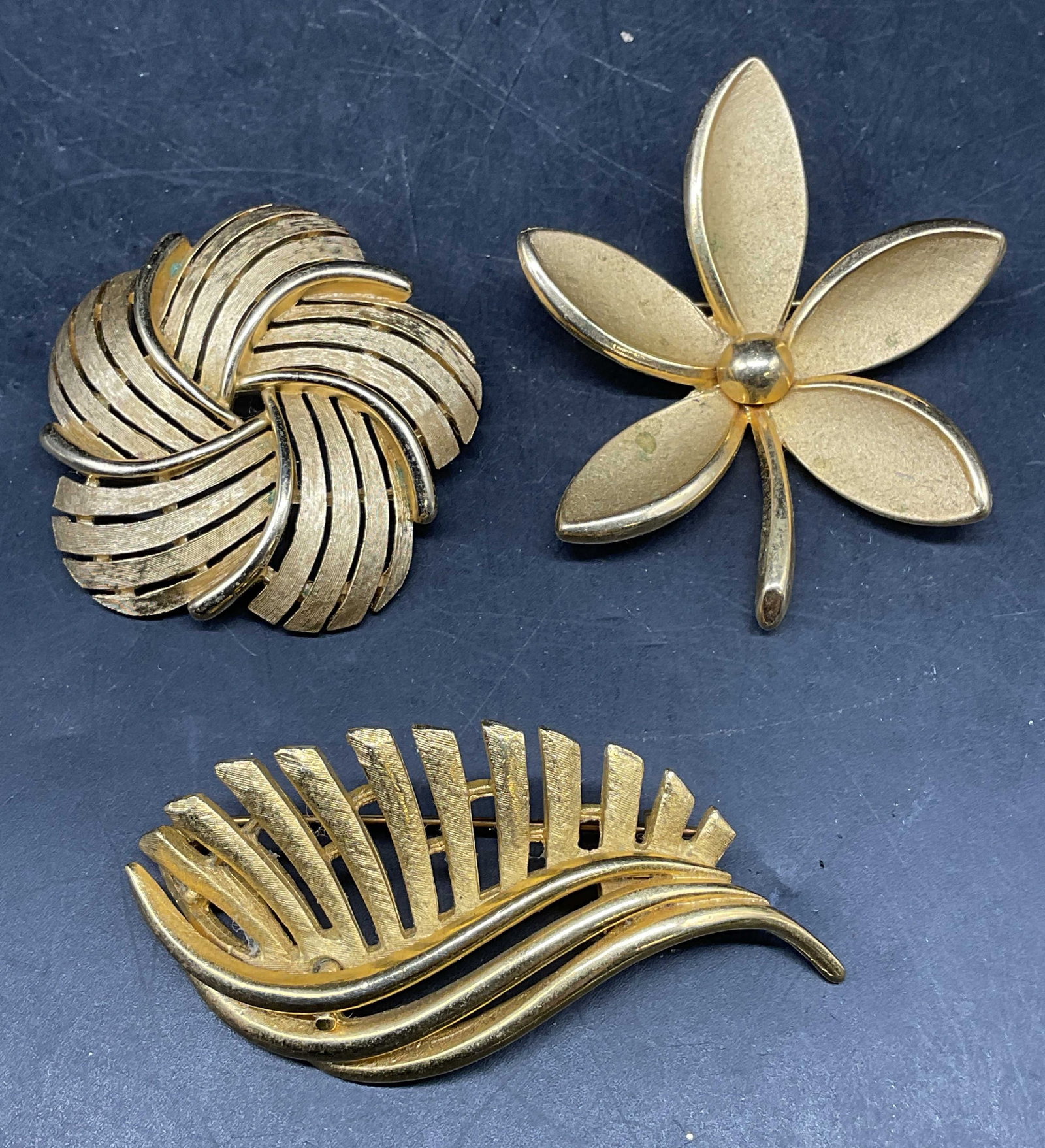 Lot 3 Trifari Gold Tone Flower Brooch +: Lot of 3 vintage gold tone brooches. 2 Trifari flower brooches. Vintage abstract curved leaf brooch. Largest measures approx. 2.5 x 1.25 inches. Some scratching. Jewelry, estate jewelry, costume