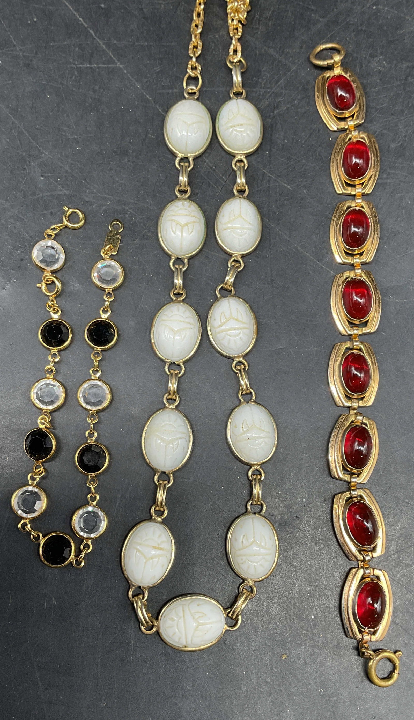 Lot 3 Gold Tone White Scarab Necklace +: Lot of 3 pieces. Vintage gold tone carved white faux stone scarab necklace. Drop length 10 inches. Chain needs untangling. Gold tone red faux stone cabochon bracelet. Measures approx. 6.5 inches