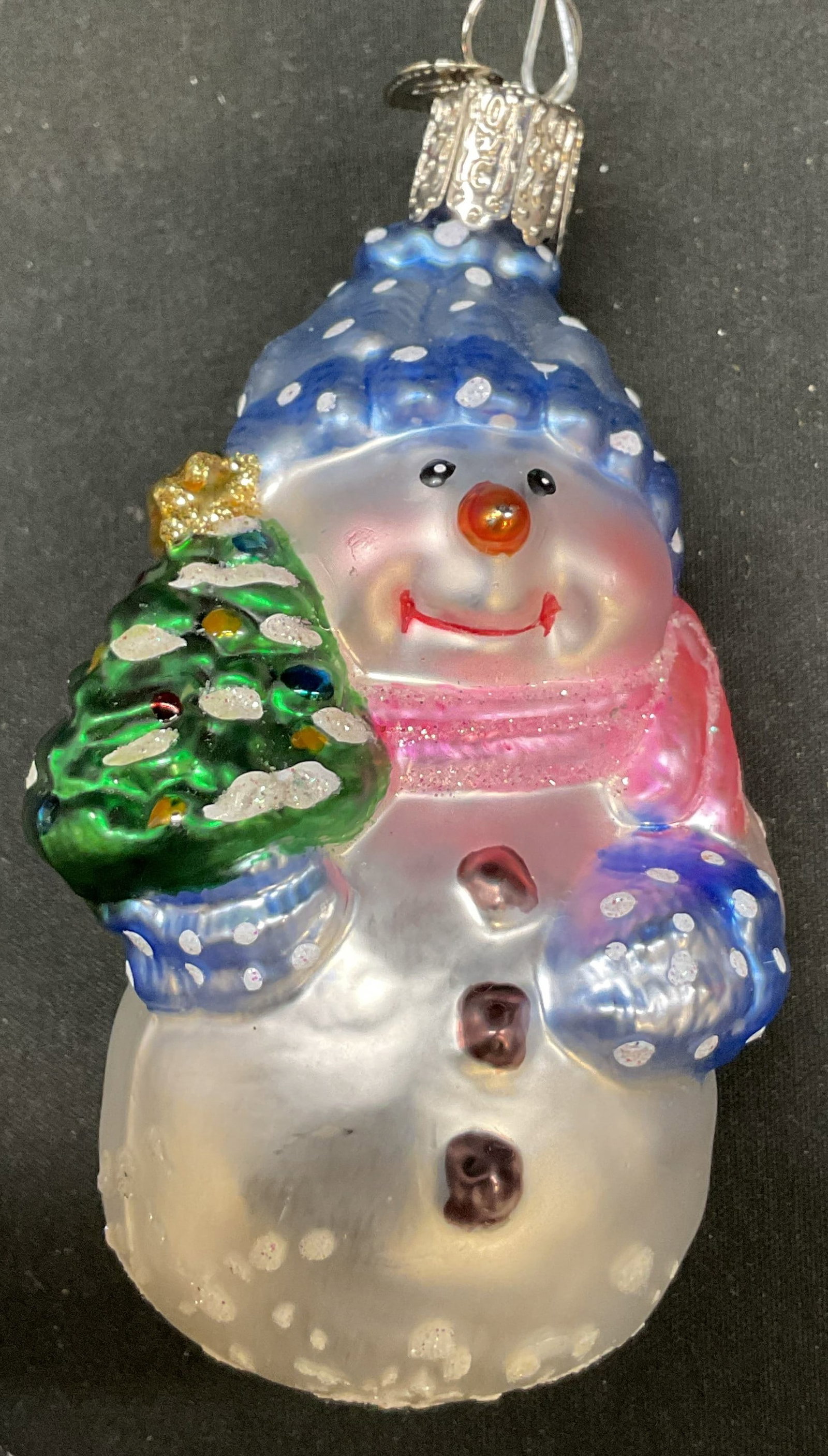 Old World Christmas Snowman Ornament: Old World Christmas snowman ornament. Blown glass. Snowman is holding a tree and wears mittens, scarf, and a hat. Varying colors and glitter accents, hand painted. Measures approx 4 inches in length.
