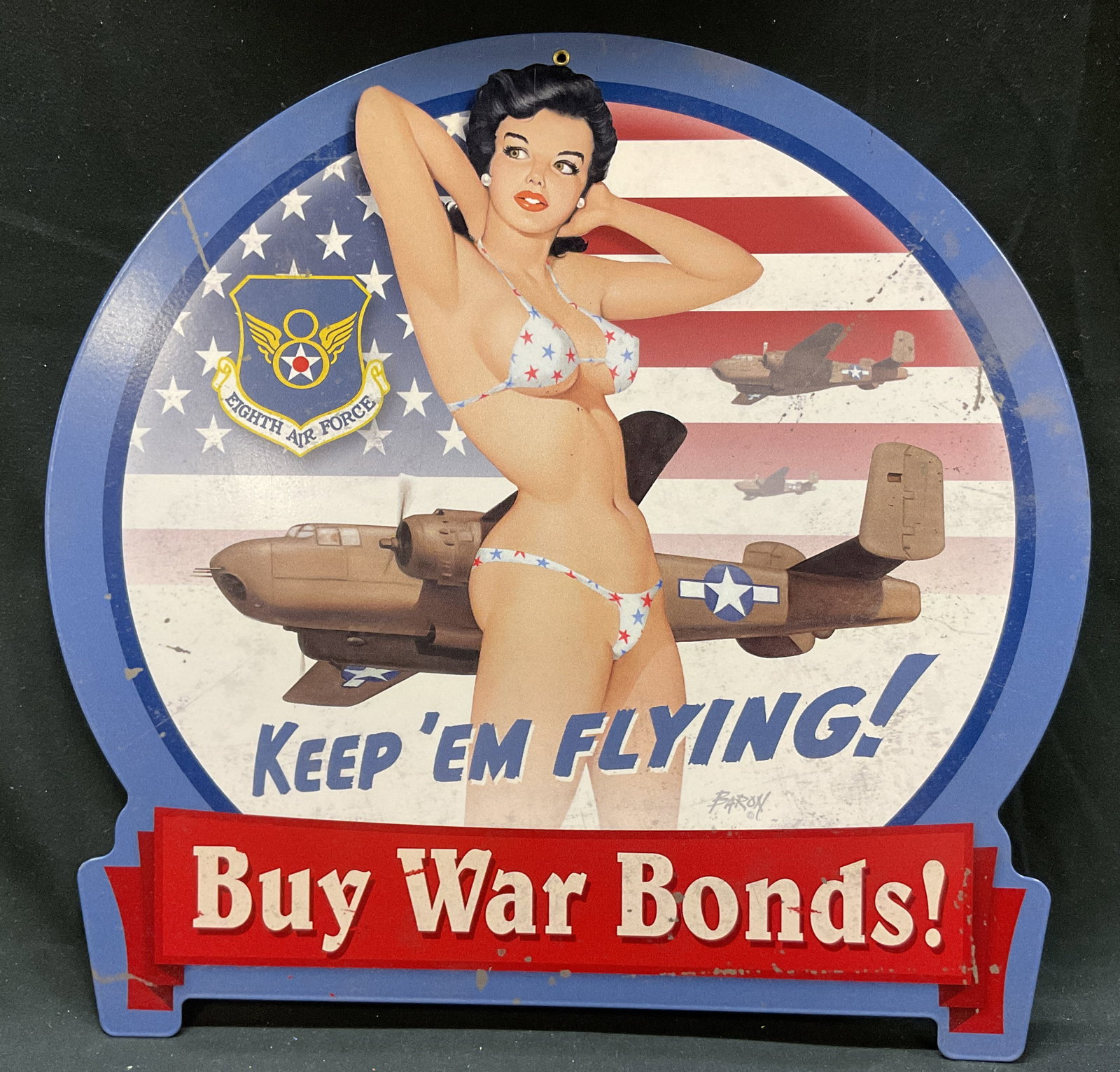 Baron Von Lind War Bonds Metal Wall Sign: Baron Von Lind war bonds metal wall sign. Marked Baron. Features a WWII inspired pin up girl and B25 bomber against an American flag. Reads Keep Em Flying Buy War Bonds. Varying colors. Measures
