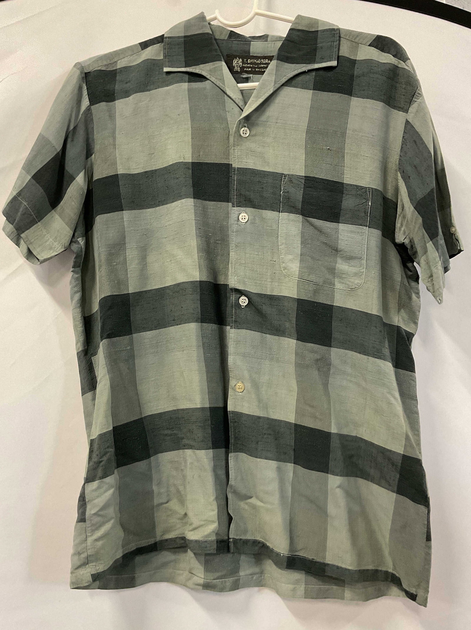 T. Shinawatra Silk Plaid Buttoned Shirt Thailand: T. Shinawatra silk plaid buttoned shirt. Made in Thailand. 100% pure silk hand woven. Short sleeve. Collared and buttoned. Front pocket. White, grey, black plaid pattern. Measures approx 18 across che