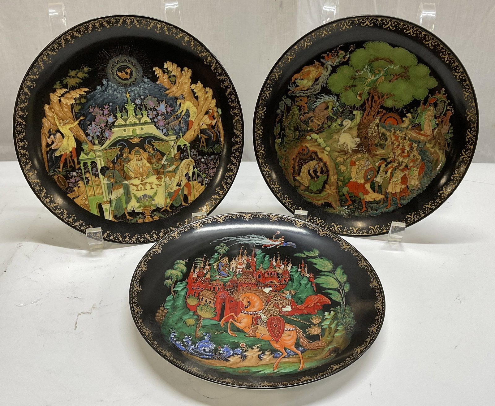 Lt3 1980s Tianex Russian Legends Plates: 3 1980s Tianex Russian Legends Decorative Porcelain Plates. Feature Painted Colorful Scenes on Black from Russian Fairy Tales with Gilt Accents. One is From 1988 and 2 are From 1989. Russian Descripti