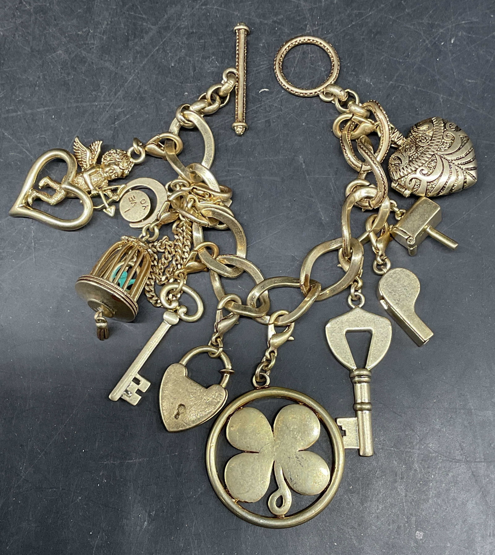 Vintage Gold Tone Statement Charm Bracelet: Vintage gold tone statement charm bracelet. Four leaf clover, cherub, key, whistle, birdcage, heart charms. Measures approx. 7.5 inches long. Some scratching. Jewelry, estate jewelry, costume