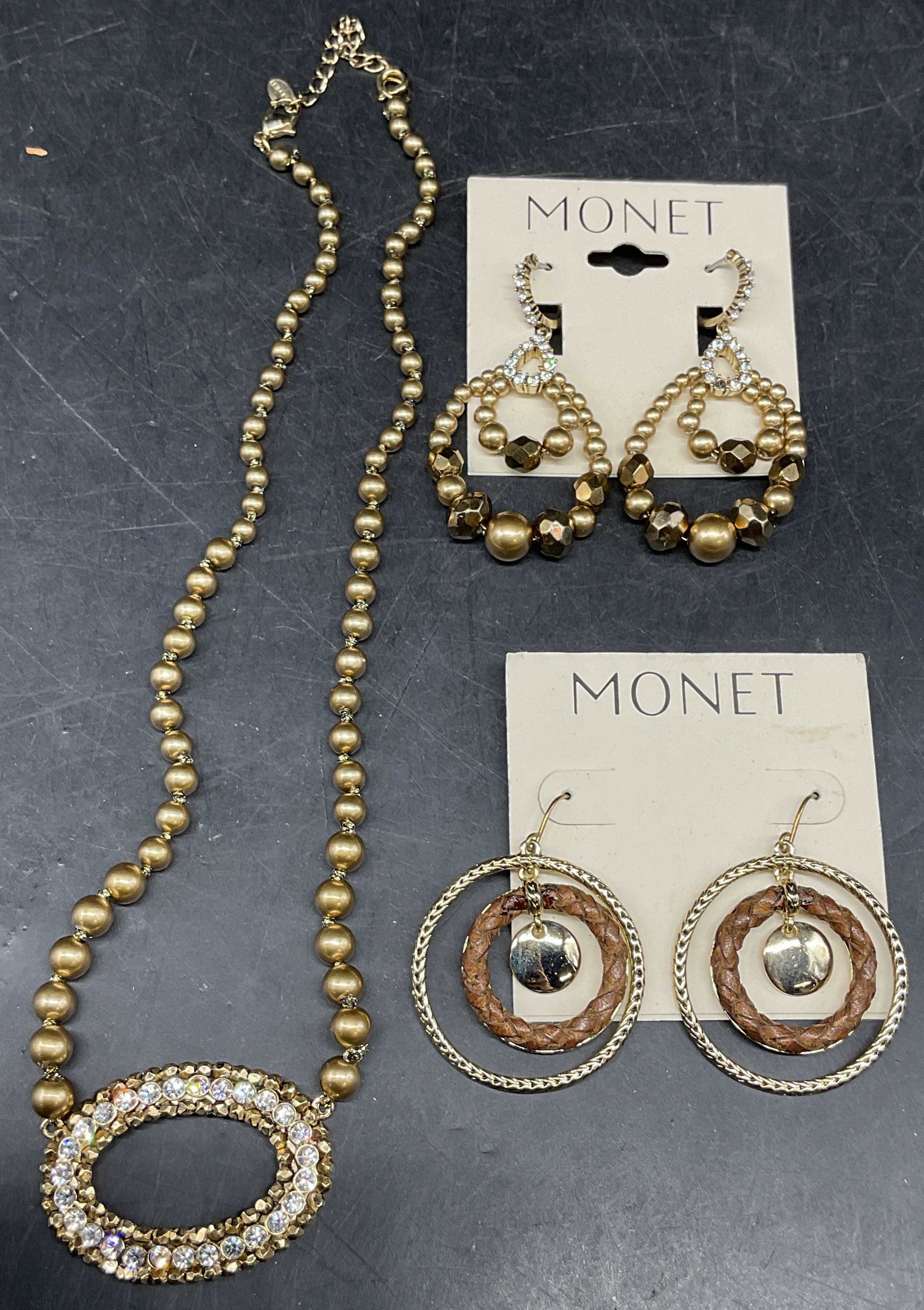 Lot 3 Vintage Monet Earrings & Necklace: Lot of 3 vintage Monet earrings and necklace. Gold tone colorless crystal and beaded earrings and gold tone open circle and braided leather earrings. Larger measures approx. 2.25 inches long. Gold