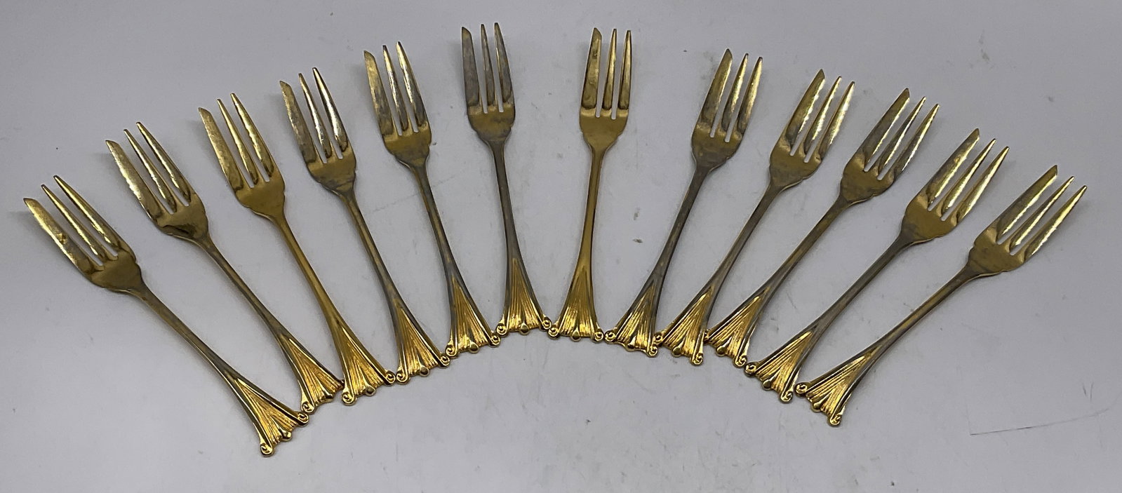 St12 Gold-Toned Silver-Plate Cocktail Forks: Set of 12 Gold-Toned Silver-Plate 3-Pronged Cocktail Forks. Marked Nickel Silver. Scratching and Fading Present. Measures app 5.25in H x 0.75in W. Gold-Toned, Gilt, Silver-Plate, 3-Pronged, Miniature