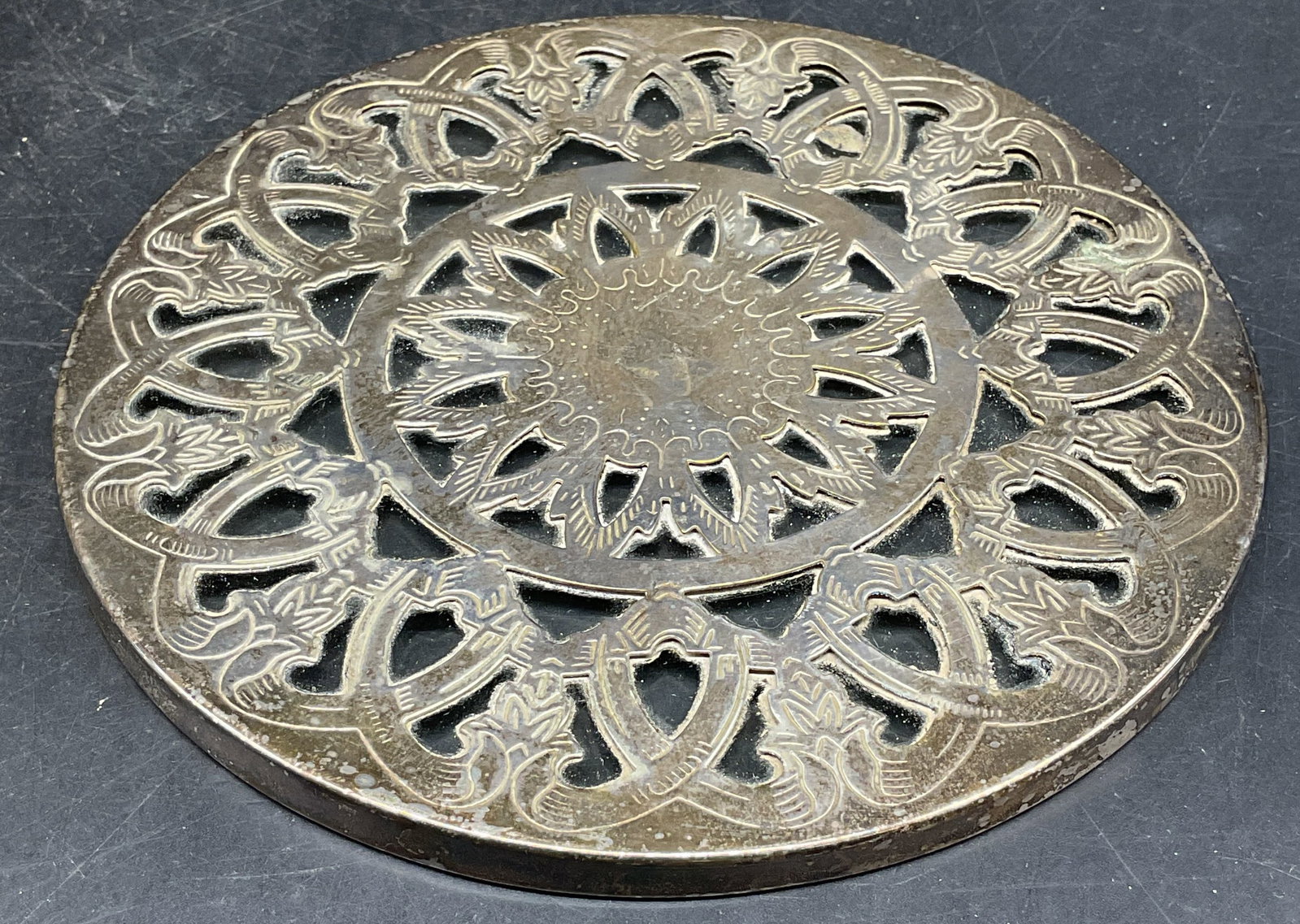 Signed Silver Plated Scroll Glass Trivet: Vintage signed silver plated and glass round trivet with ornate scroll pattern. Signed illegibly. Measures approx. 6.25 inches wide. Wear including scratching, patina, metal loose from glass. Silver p