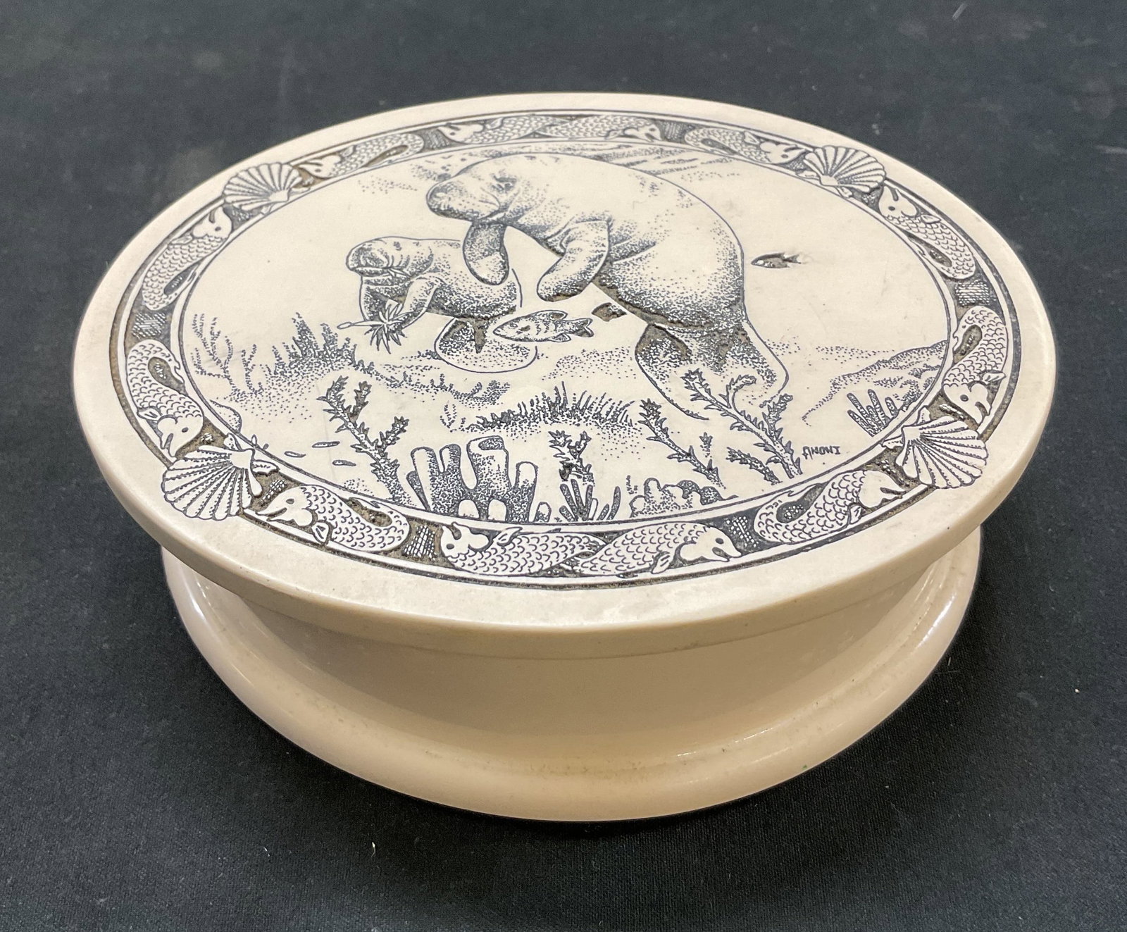 Vintage Scrimshaw Style Resin Lidded Trinket Box: Vintage Scrimshaw style resin lidded trinket box. Oval shaped. Etched scene of two manatees swimming amongst sea vegetation. Fish and shell motifs. Signed, reads illegibly. Measures approx 4 x 5.5 x