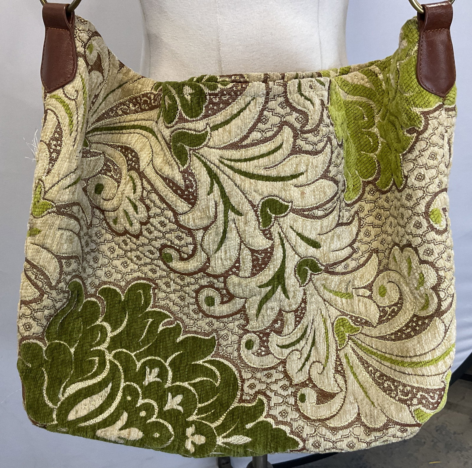 Kushmina Fabric Floral Shoulder Bag: Kushmina fabric floral shoulder bag. Brown leather strap with decorative circle accent. Brown, green, and white floral motifs. Blue lining and fitted compartments. Measures approx 14.5 x 19.5 inches. 