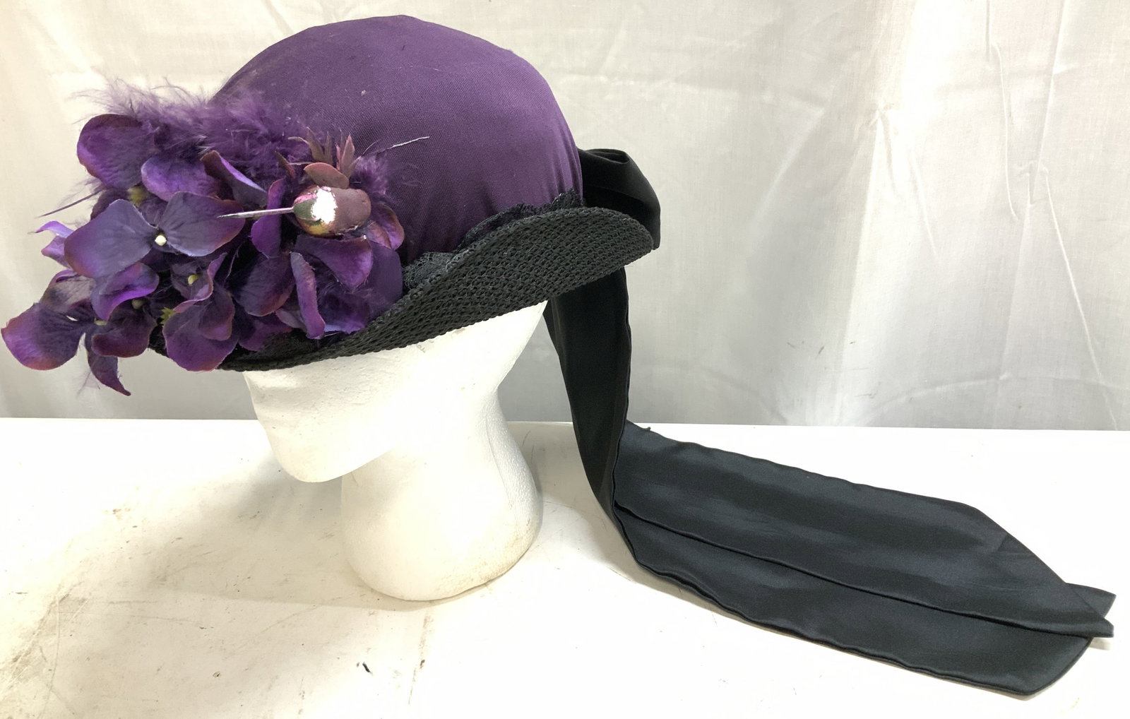 Vtg Elsie Massey Purple Evening Hat W Floral Trim: Elegant vintage ladies hat featuring a deep purple crown accented with faux violets, feathers & a satin ribbon bow tie. Ladies hat features a black brim. Property of historic Bartow-Pell Mansion Museu