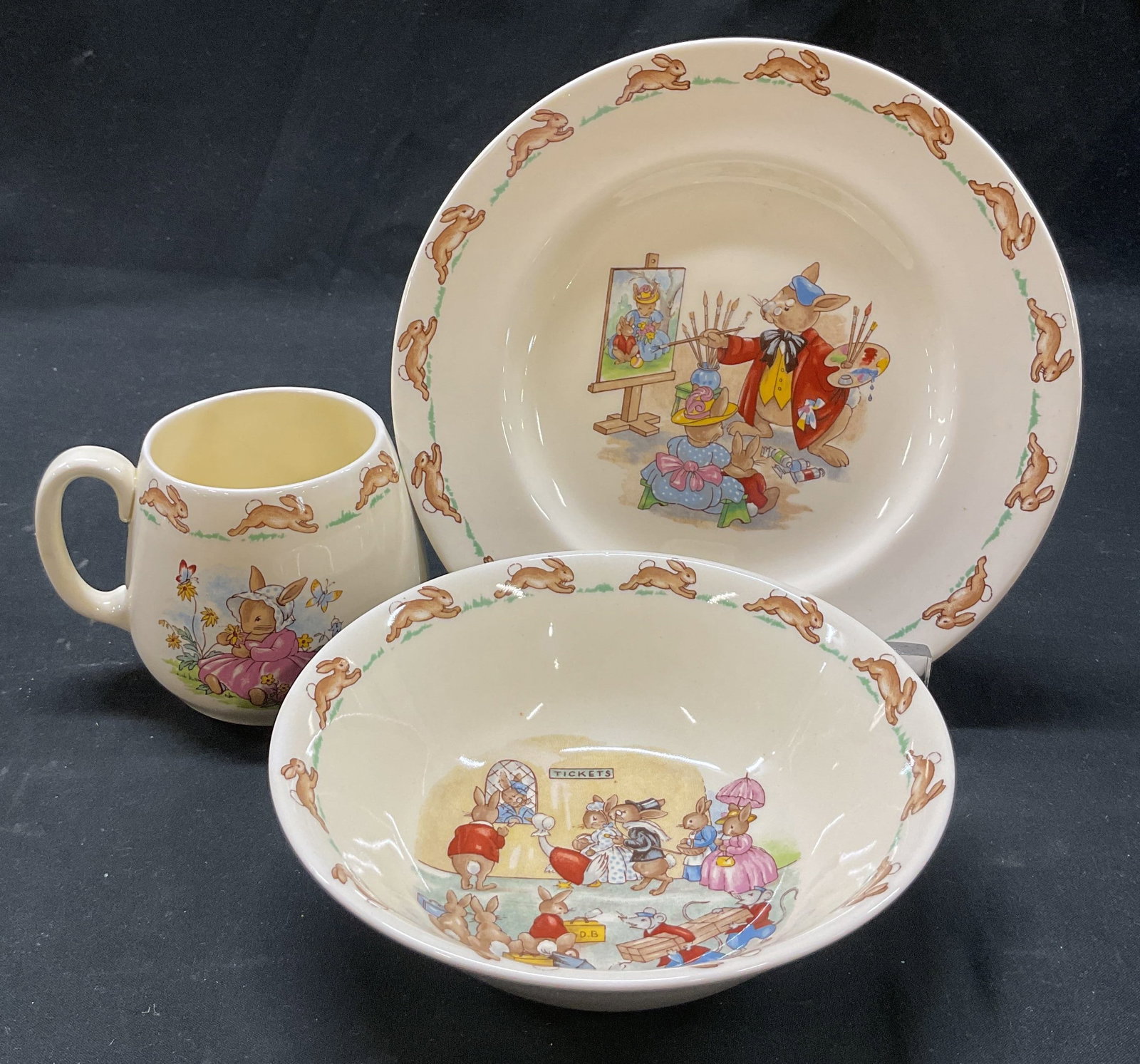 Set 3 Royal Doulton Bunnykins Tableware England: 3 piece Royal Doulton Bunnykins bone china tableware set. Marked on underside, reads Made In England Royal Doulton Bunnykins. Includes 1 bowl, 1 plate, and 1 mug. Bunnykins collection, motifs of bunni
