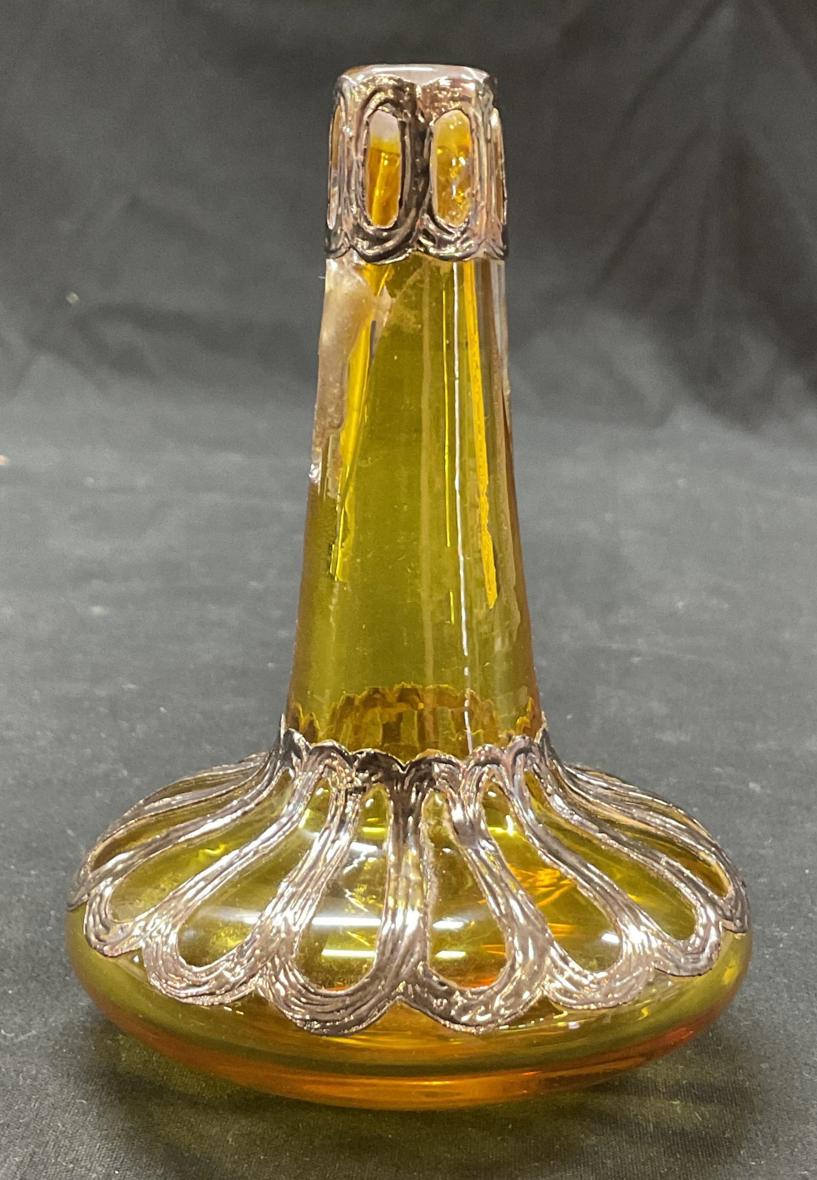1991 Sam Glass Sterling Overlay Amber Bud Vase: Sam Glass hand blown sterling silver overlay amber art glass bud vase. Marked Sam Glass 1991 on underside. Round wide base and slender neck. Ornate sterling overlay design. Measures ht approx 4.5 inch