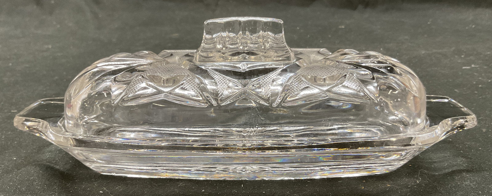 Vintage Cut Glass Butter Dish With Lid: Vintage cut glass butter dish. Comes with lid. Decorative finial on lid. Cut star and fan patterns. Textured surface. Handles on either side of dish. Starburst design on underside. Measures approx 8 1