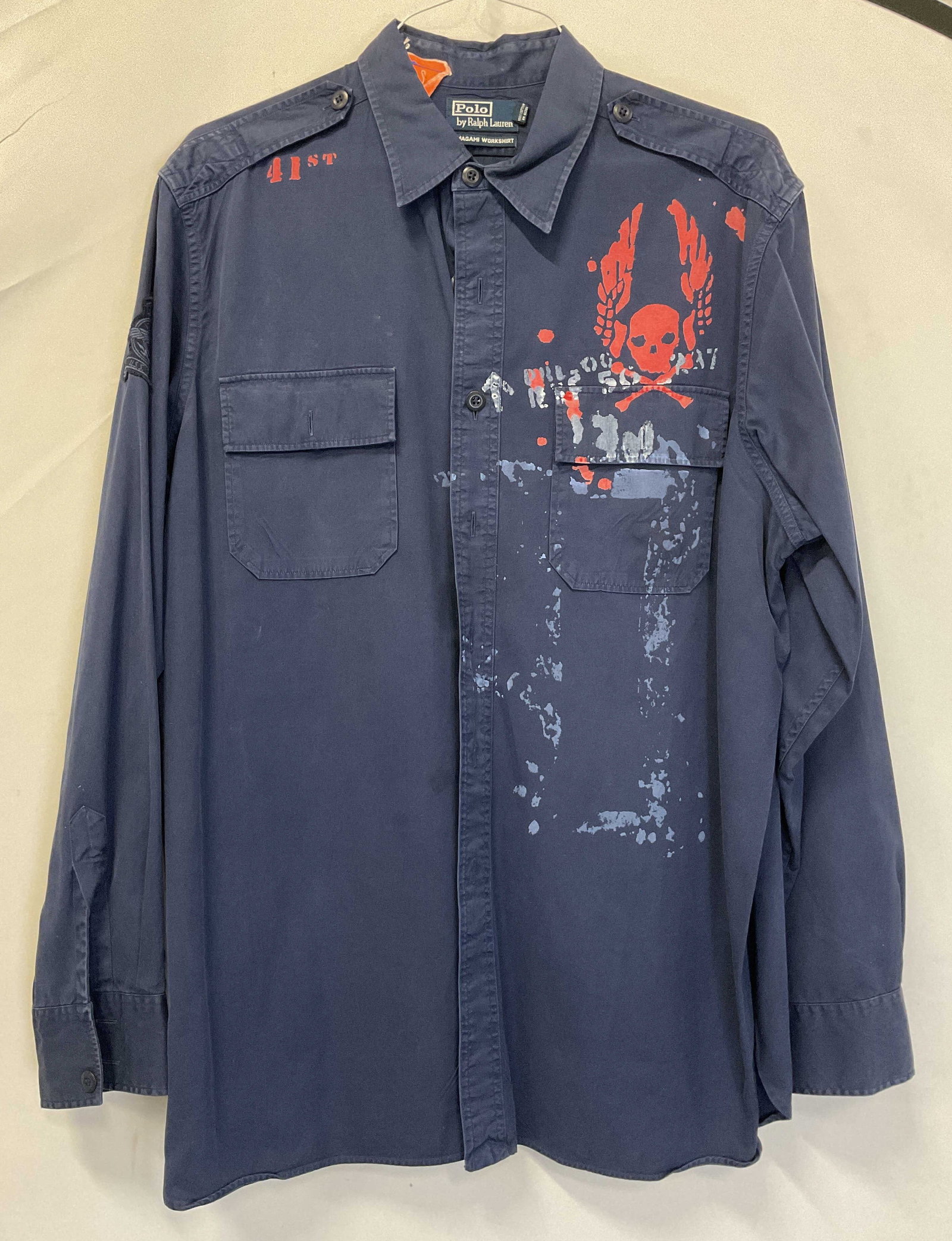 Polo Ralph Lauren Blue Skull Button Down: Polo Ralph Lauren blue skull button down. Size XL. 100% cotton. Temagami Workshirt. Collared and buttoned. Long sleeve. Front pockets. Skull with wings design in red. Shirt also has a design that read