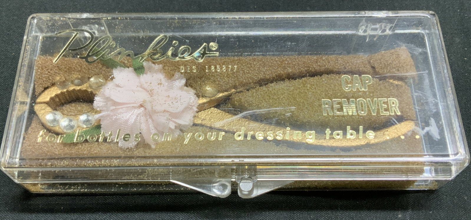 Vtg Plinkies Dresser Cap Remover W Org Box: Vintage Plinkies cap remover designed to help open bottles on a dressing table. Cap remover is embellished with rhinestones & a pink floral accent. Gilt toned. Comes with original box. Surface wear co