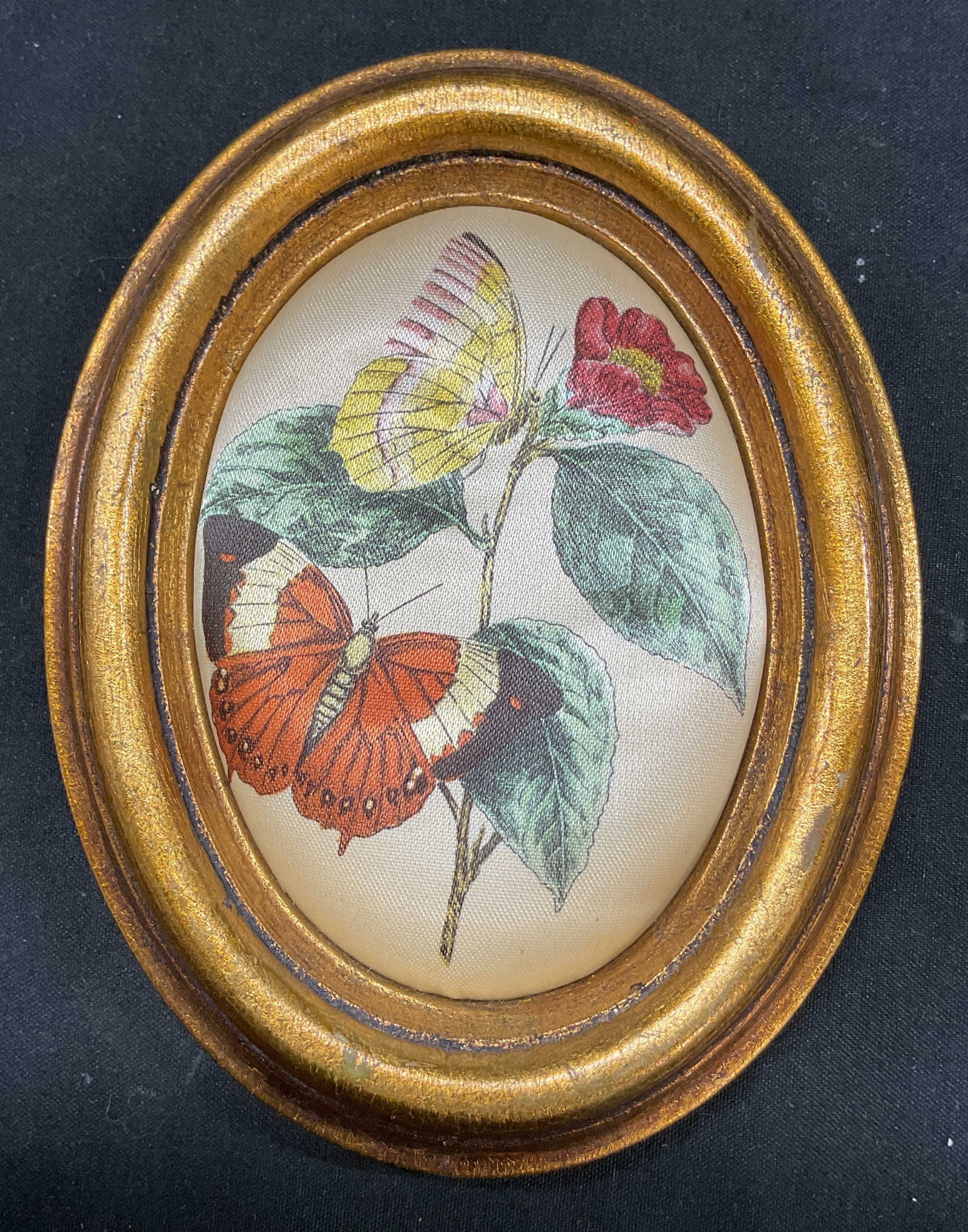 Vintage Framed Botanical Wall Decor: Vintage framed botanical wall decor. Oval shaped gilt wood frame. Cushioned butterfly and floral motifs in varying colors. Measures approx 4 x 5 inches. Surface wear consistent with exposure. Wall dec