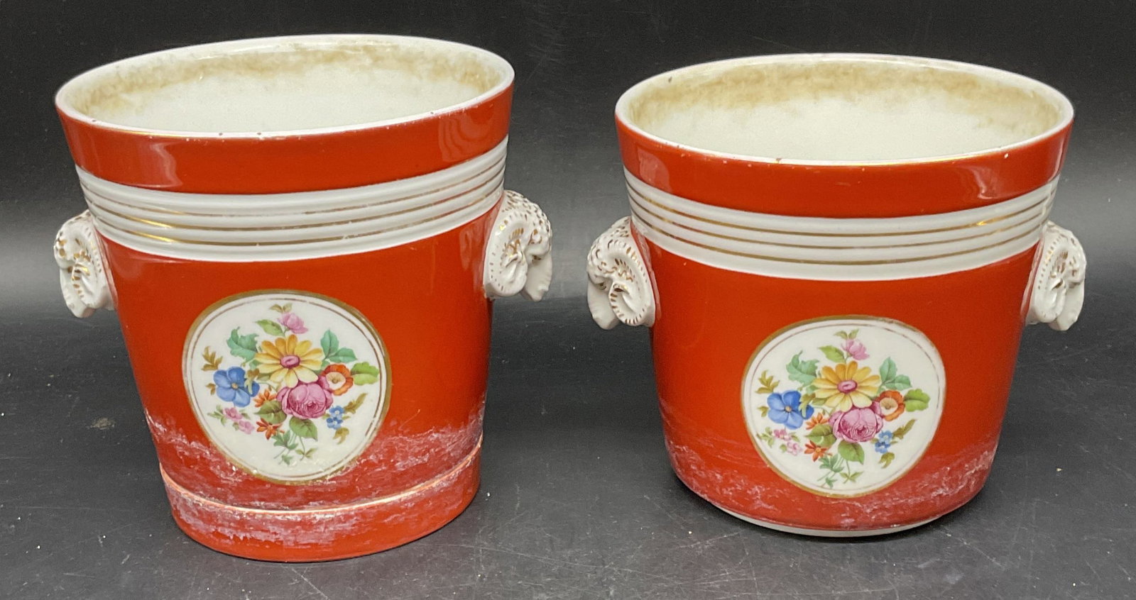 Pair Red Porcelain Floral Ram Head Cachepots: Pair of porcelain cachepots, one with under plate. Hand painted floral designs with gilt borders and rams head finials. Cachepots measures approx. 5.5 x 5 inches. Wear including crazing, loss to paint