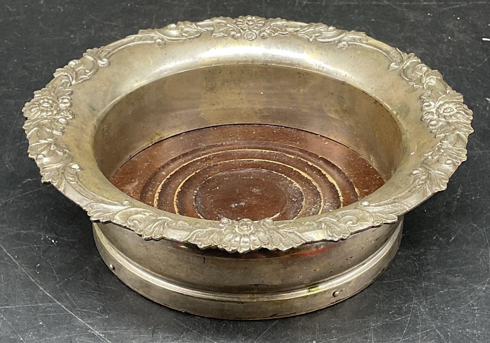Vintage Silver Plated Wine Bottle Coaster: Vintage heavy silver plated wine bottle coaster. Wood base. Raised floral rim. Measures approx. 6.25 x 2 inches. Wear including patina and scratching. Wine bottle coaster, silver plated coaster, bar a