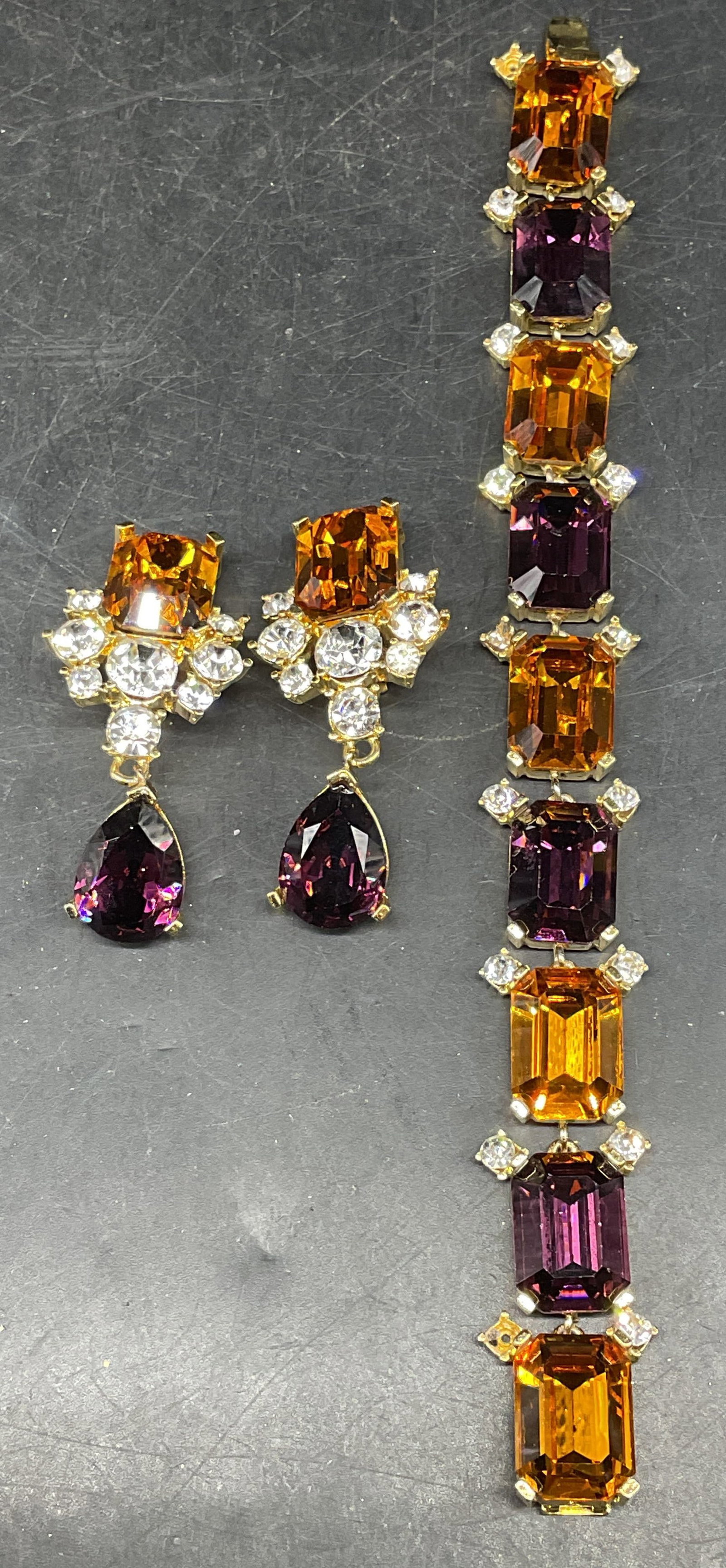 Set 2 Todd Anthony Orange Rhinestone Jewelry: Set of 2 pieces vintage matching Todd Anthony gold tone purple, orange, and colorless rhinestone jewelry. 1 pair of earrings and 1 bracelet. Bracelet measures approx. 7.5 inches. Earrings measures app