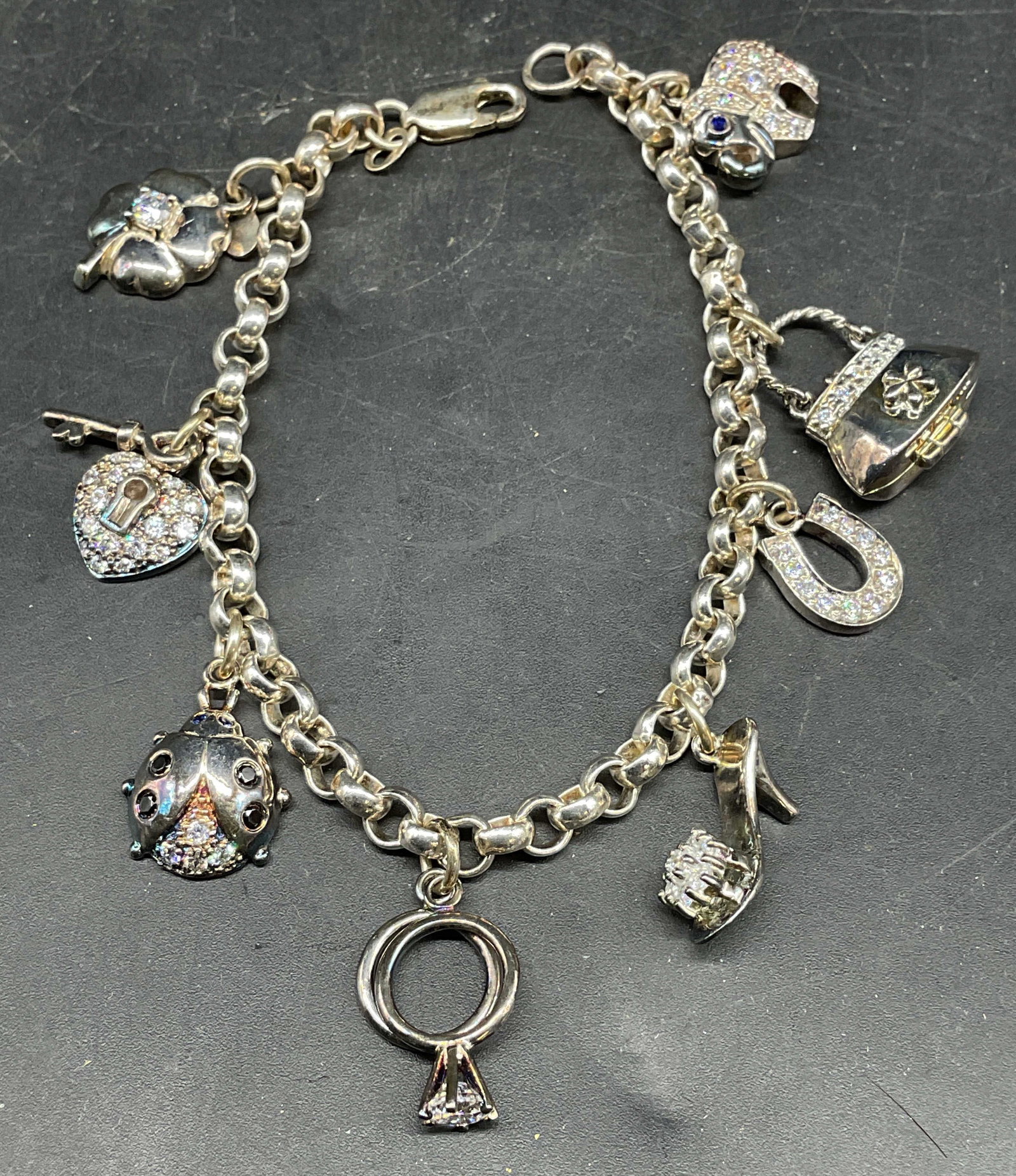 Signed Sterling Silver Rhinestone Charm Bracelet: Signed Sterling silver charm bracelet with rhinestone accents. Heart, ladybug, ring, horseshoe, heel, and more charms. Marked sterling. Measures approx. 7 inches long. Total weight 28.6 grams. Signed 