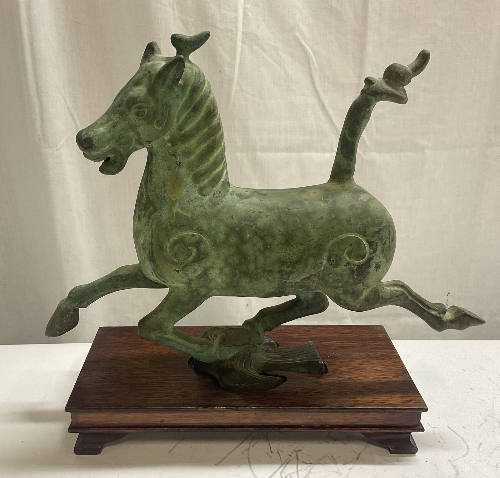 VTG Bronze Flying Horse of Gansu Replica Statue: Vintage Bronze Han Dynastys Flying Horse of Gansu Replica Statue on Wooden Stand. Verdigris Patina. Depicts a Horse Galloping on a Swallow. HS Significant Weight. Condition Consistent With Exposure. M