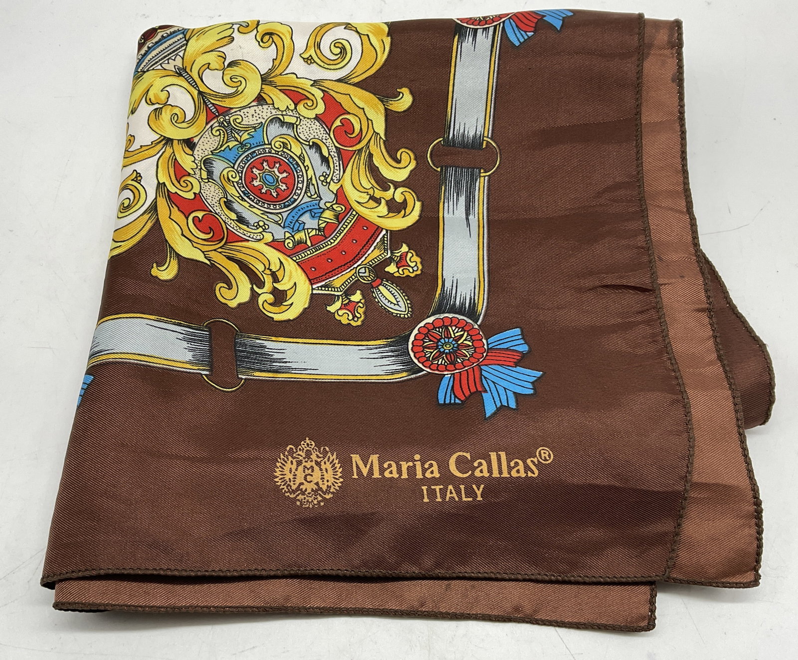 VTG Maria Callas Designer Silk Scarf ITALY: Vintage Maria Callas Designer Silk Scarf. Brown with Red, Gold, Blue, White, and Silver Equestrian and Baroque-Style Print of Buckles, Shields, Crests, and Ribbons. Made in Italy. Some Staining. Measu