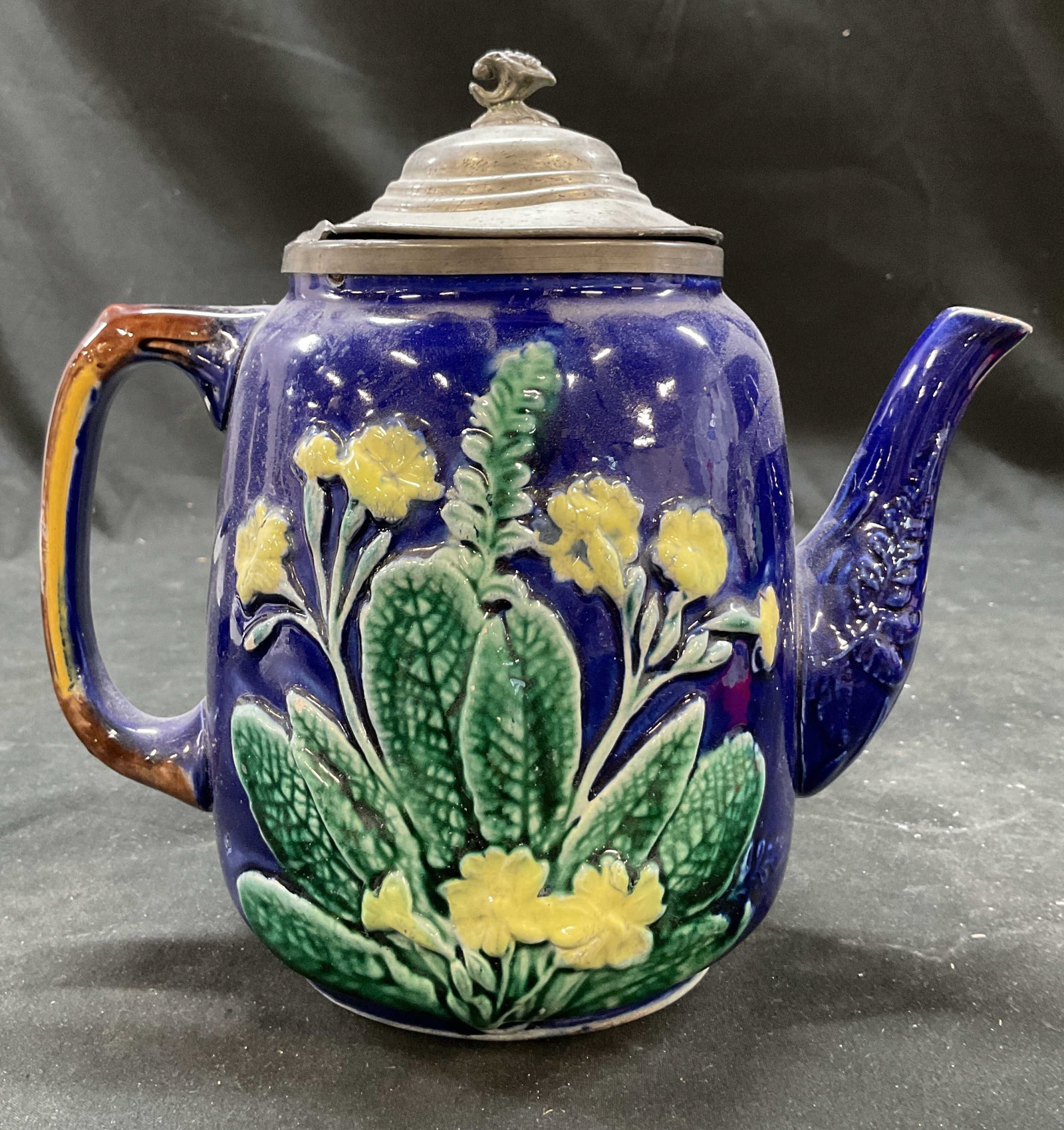 C1874 WEDGEWOOD Majolica Pitcher, Eng: Antique Majolica WEDGEWOOD Pitcher dating from 1874, featuring relief molded primroses and ferns on a cobalt blue ground, it includes a hinged pewter lid with detailed floral and leaf motifs property 