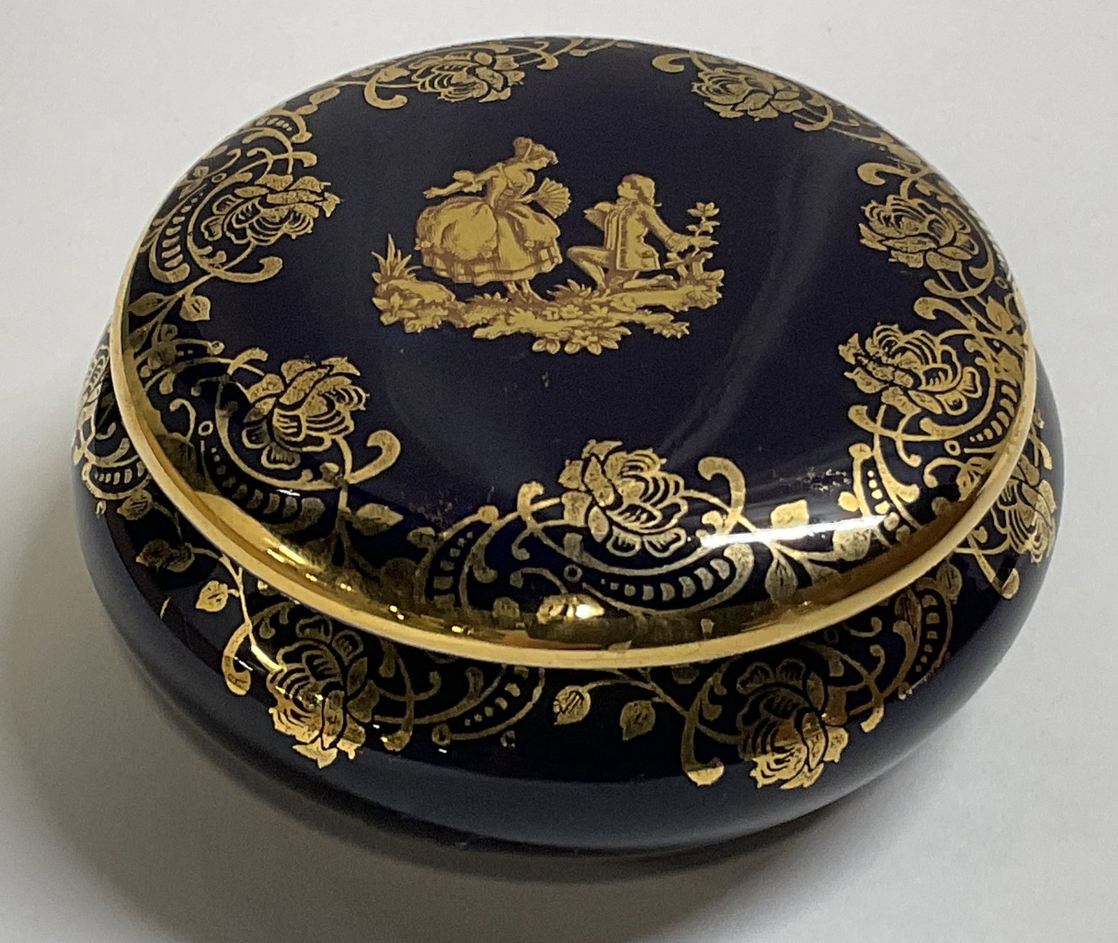 VTG Limoges Courting Scene Porc Trinket Box FRANCE: Vintage Limoges Trinket Box. Cobalt Blue Glaze with Gilt Courting Scene and Floral Design. Made in France. Condition Consistent With Exposure. Measures app 2in H x 3in Diam. Vintage Trinket Box, Limog