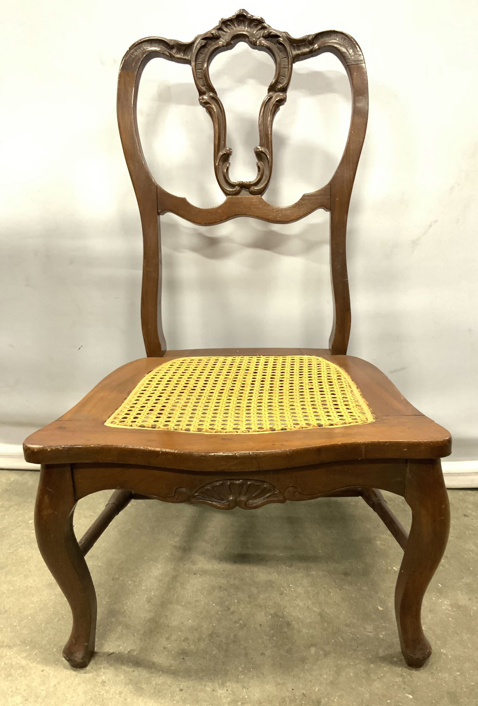 Vtg Louis XV Low Crvd Wood Chr W Caned Seat: Chair is vintage and wooden. Piece has Louis XV style with scrolled detail within wooden frame. Chair is light brown toned with tan toned caned seat area. Chair has 4 wooden legs with H form stretcher