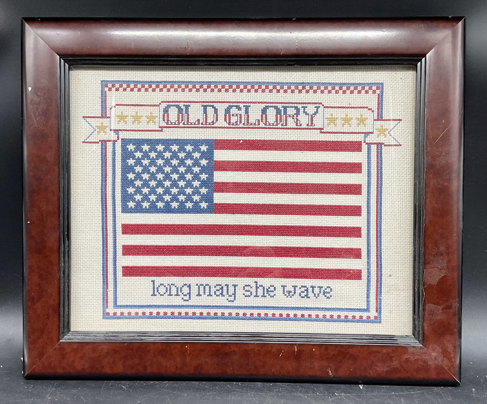 Framed Old Glory American Flag Cross Stitch Panel: Framed cross stitch panel. Old Glory Long May She Wave. American flag. Wood frame. Not examined out of frame. Frame measures approx. 14.25 x 17.25 inches. Some wear consistent with exposure. Cross sti