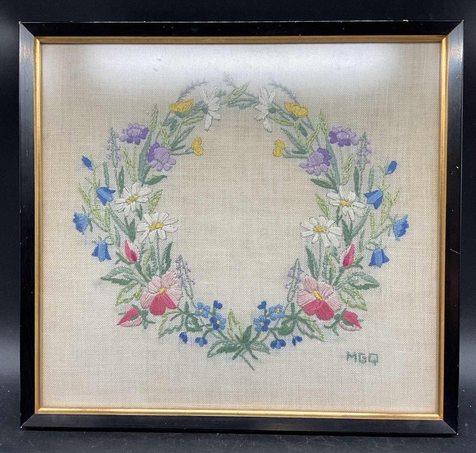 MGQ Floral Wreath Hand Embroidered Panel: Framed hand embroidered panel. Signed lower right MGQ. Floral wreath. Wood frame. Not examined out of frame. Frame measures approx. 14 x 15 inches. Some wear consistent with exposure. Embroidered pane