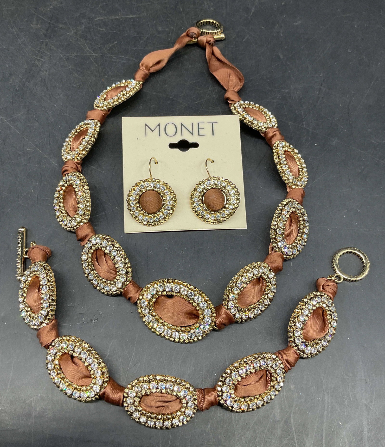 Lot 3 Monet Gold Tn Necklace, Bracelet & Earrings: Lot of 3 vintage matching Monet jewelry set. Gold tone and rhinestone brown satin ribbon necklace, bracelet, and earrings. Necklace drop length 6.5 inches, bracelet measures approx. 7.5 inches, earrin