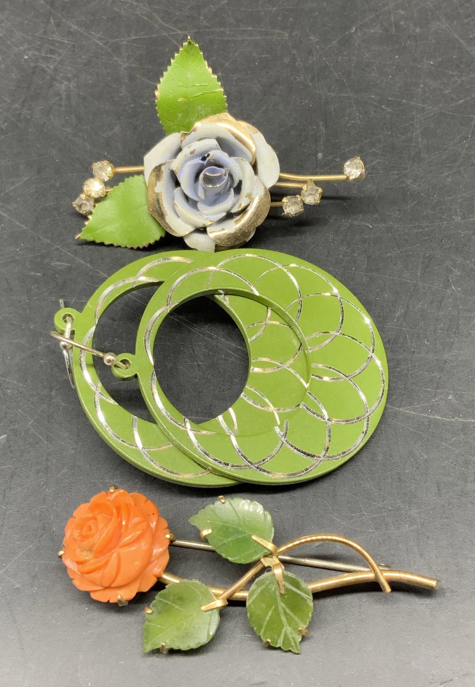 Vintage Green Jewelry Brooches and Earrings: Lot three vintage jewelry pieces, includes green enamel hoop earrings, green white enamel and rhinestone gold toned floral brooch and green orange glass gold toned floral stem brooch, largest measures