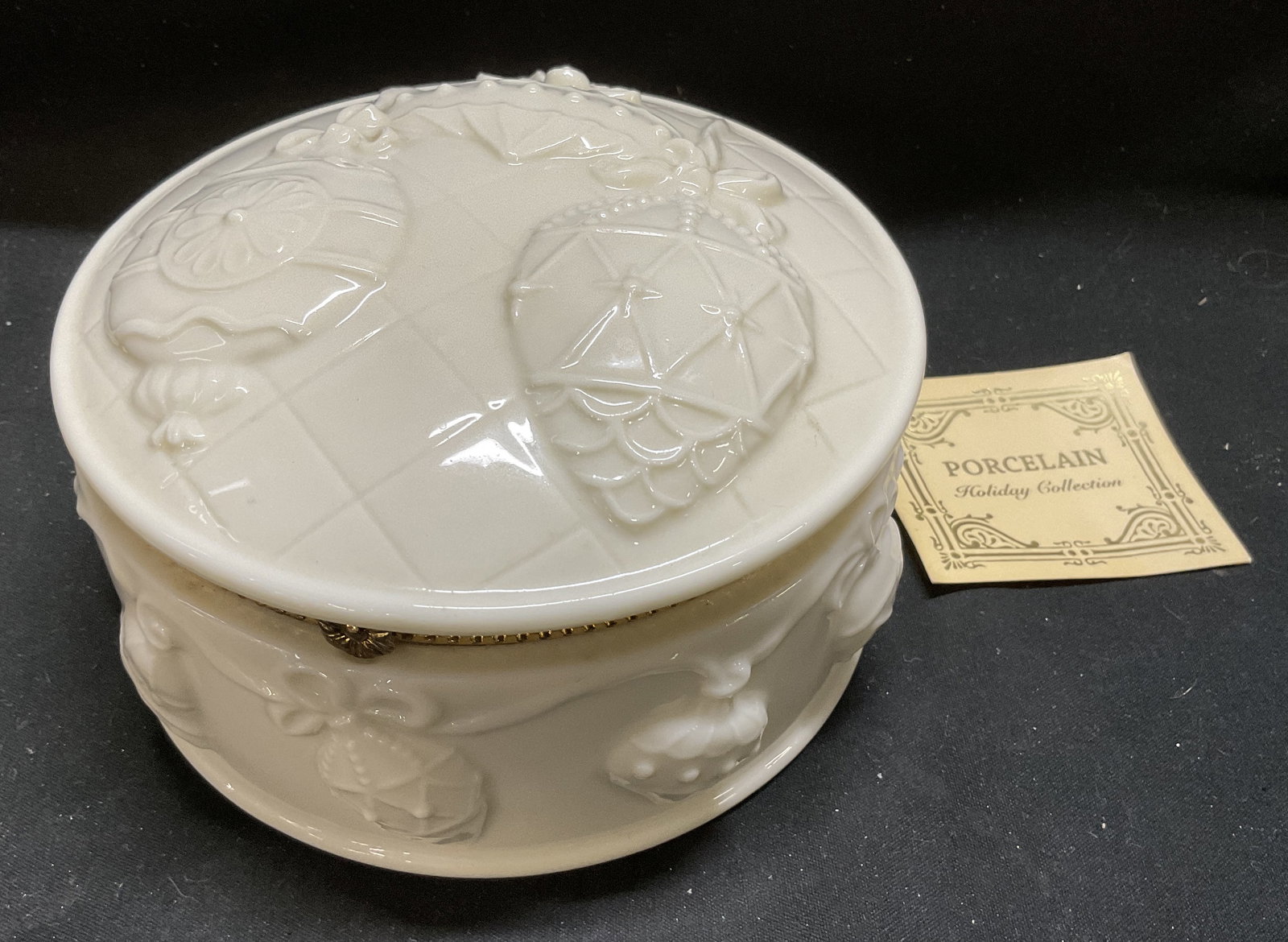 VTG Ornament Design Porc Mirrored Trinket Box: Vintage Cream Porcelain Mirrored Trinket Box. Features Raised Christmas Ornament Designs with Diamond Lattice Background on Lid. Garland Border of Ornaments and Bells on Side. Opens on Gold-Toned Meta