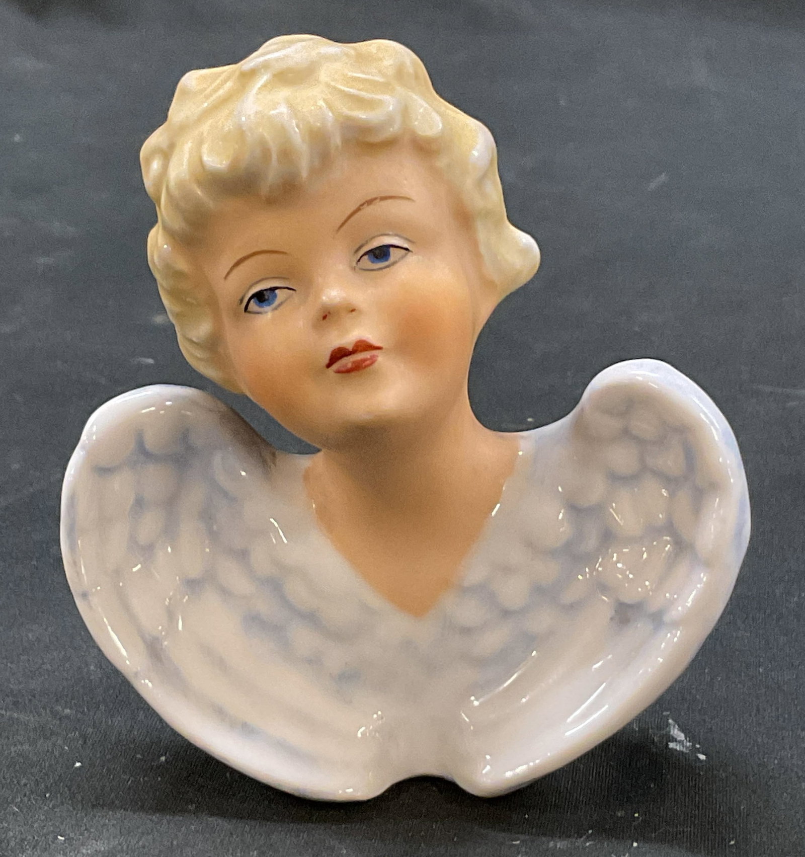 Alfred Orlik Porcelain Cherub Figure Germany: Alfred Orlik porcelain cherub figure. Marked Orlik Germany on underside. Cherub figure with blue wings, blonde hair, blue eyes, and red lips. Hand painted. Textured surface and scalloped edge.