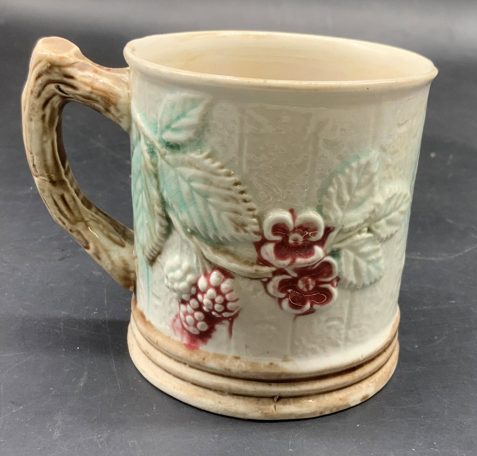 Antique English Majolica Ceramic Mug: Antique English majolica ceramic mug, featuring a molded blackberry and leaf design, measures ht 3.5 inches, faux bois branch form handle , handle to rim app 4 inches, property of former Manhattan