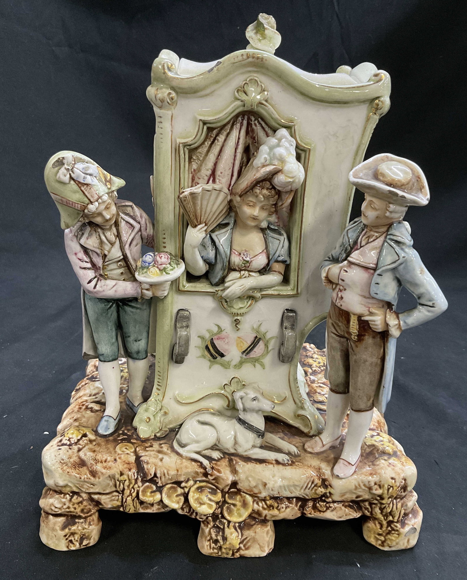 VTG Porc Rococo Sty Courtship Scene Figural Jar: Painted Porcelain Rococo Style Courtship Scene Figural Jar. Depicts Woman in Sedan Chair Fanning Herself With Two Male Suitors and a Dog Outside. Rocky Stone Style Base. Lid on Chair Opens to Reveal C