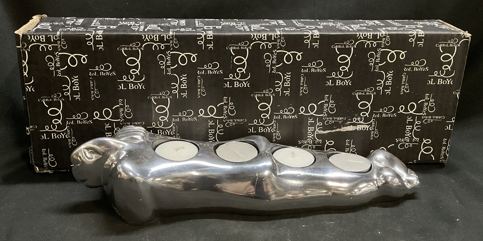 Carrol Boyes Lounger Tealight Holder S.AFRICA: Carrol Boyes Silver-Toned Cast Aluminum Surrealist Lounger Tealight Holder. Made in South Africa. Features a Stylized Woman Laying on Stomach with Hand Over Her Shoulder. Comes with Original Box and P