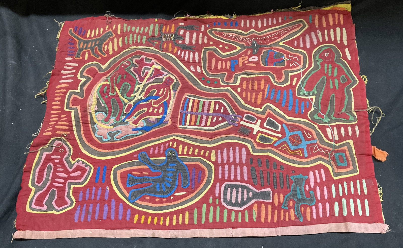 Panamanian Guna Mola Textile Art: Panamanian Guna Mola Textile Art. Red with Hand-Stitched Reverse Applique. Colorful Stylized Figures, Animals, and Helicopter Motifs. Some Staining. Measures app 20in L x 14.5in W. Panamanian,